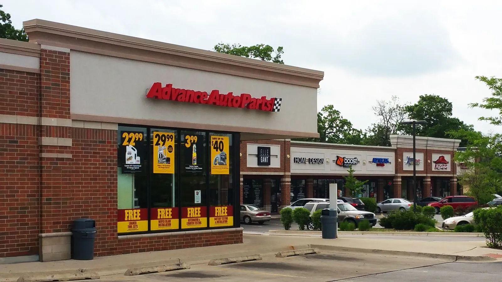 Advance Auto Parts storefront in a strip mall, with red signage and parked cars in front.