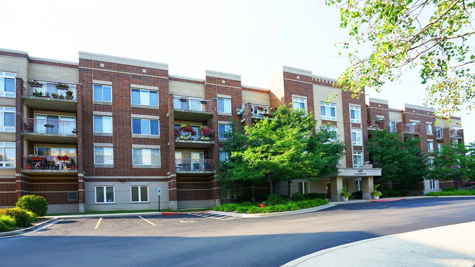 Brick apartment building with balconies along a tree-lined street on a sunny day