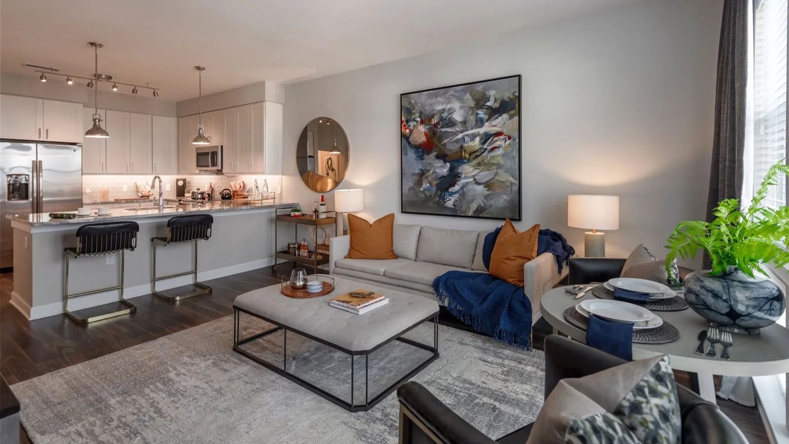 Modern open-plan living room with gray sofa, coffee table, kitchen island, and abstract wall art