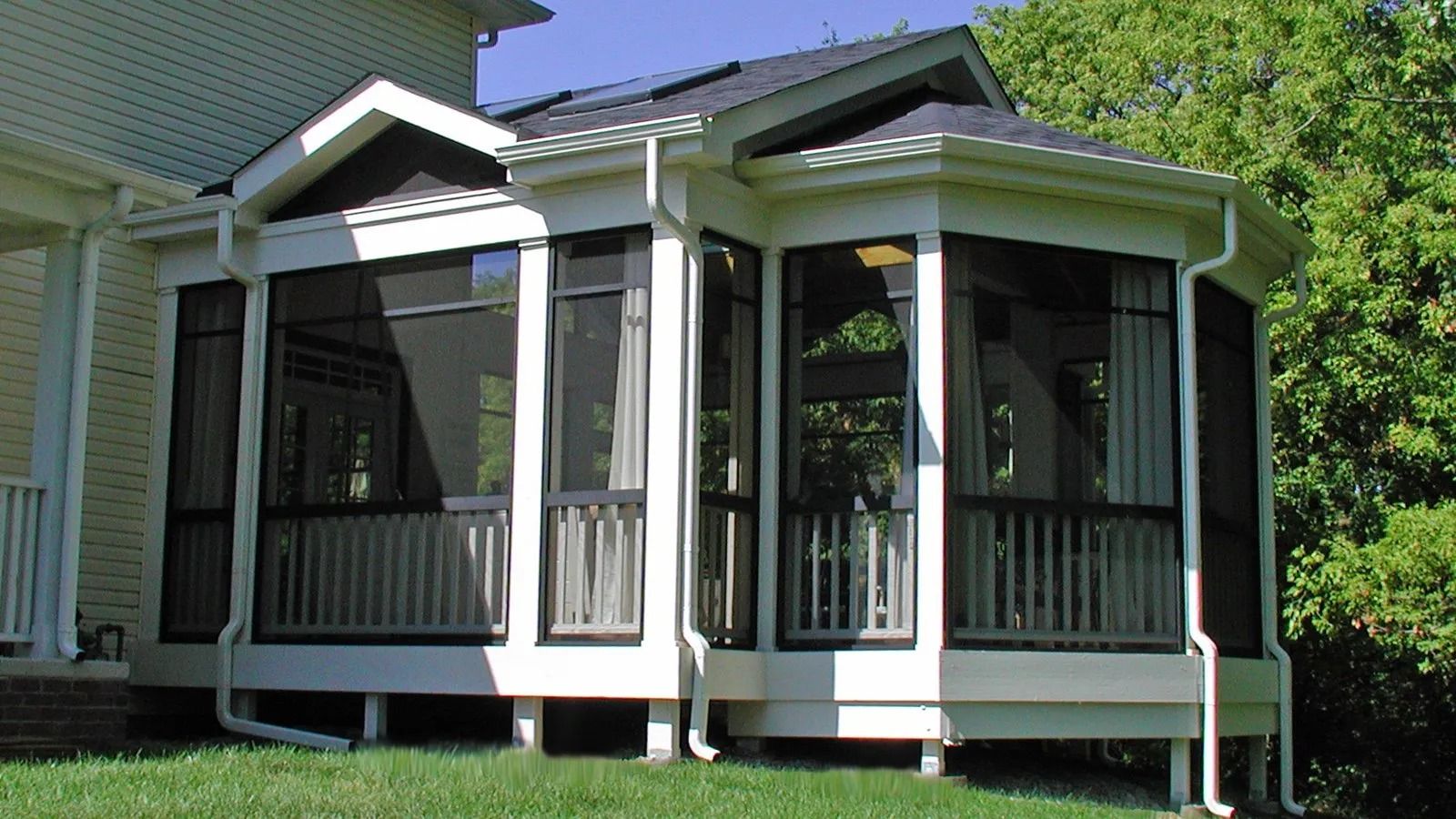 White house porch with screened windows, columns, and a small front deck surrounded by greenery