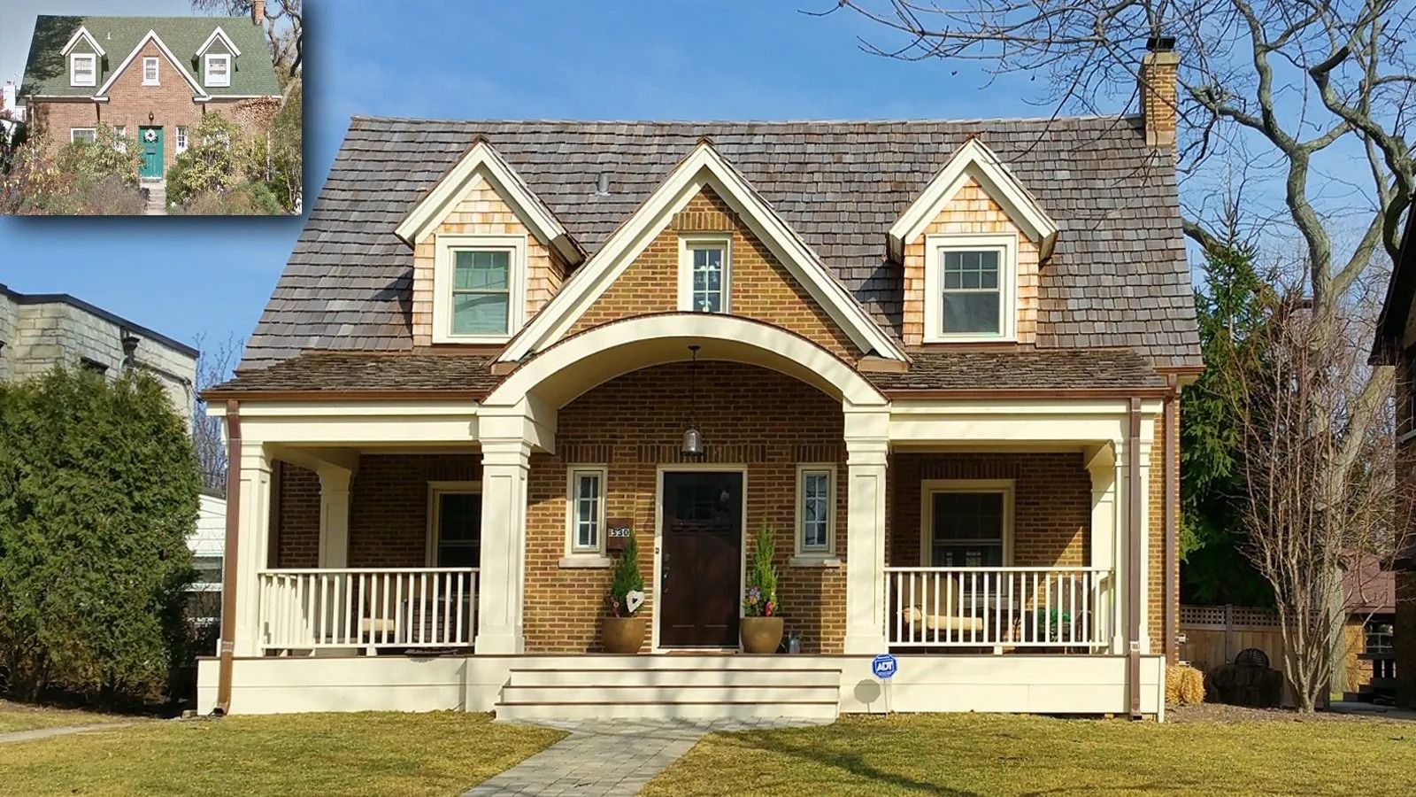 Brick house with cream porch, gabled roof, and dormer windows under a clear blue sky.