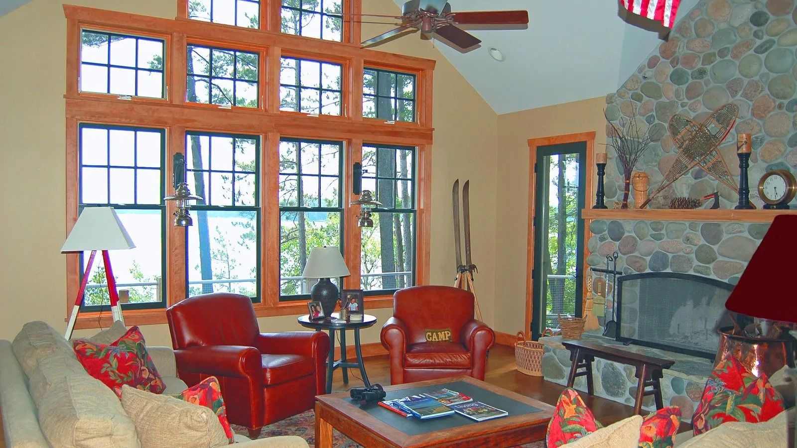 Cozy living room with red chairs, large windows, stone fireplace, and vaulted wood ceiling.