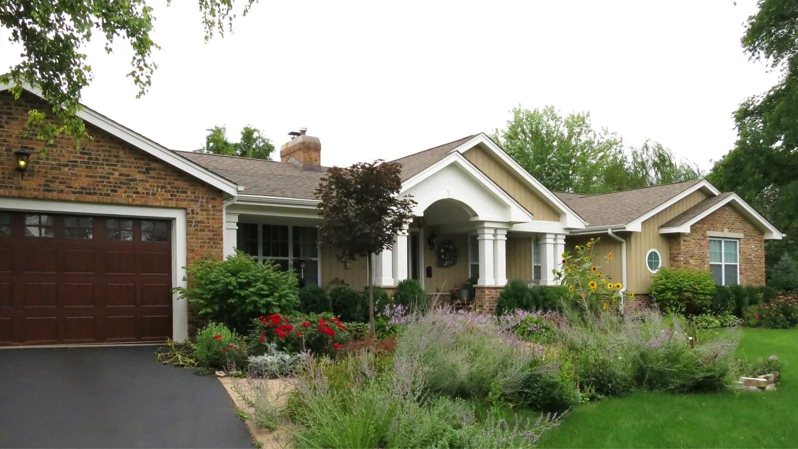 Suburban brick house with garage, white porch columns, and a front yard of flowers and ornamental grasses