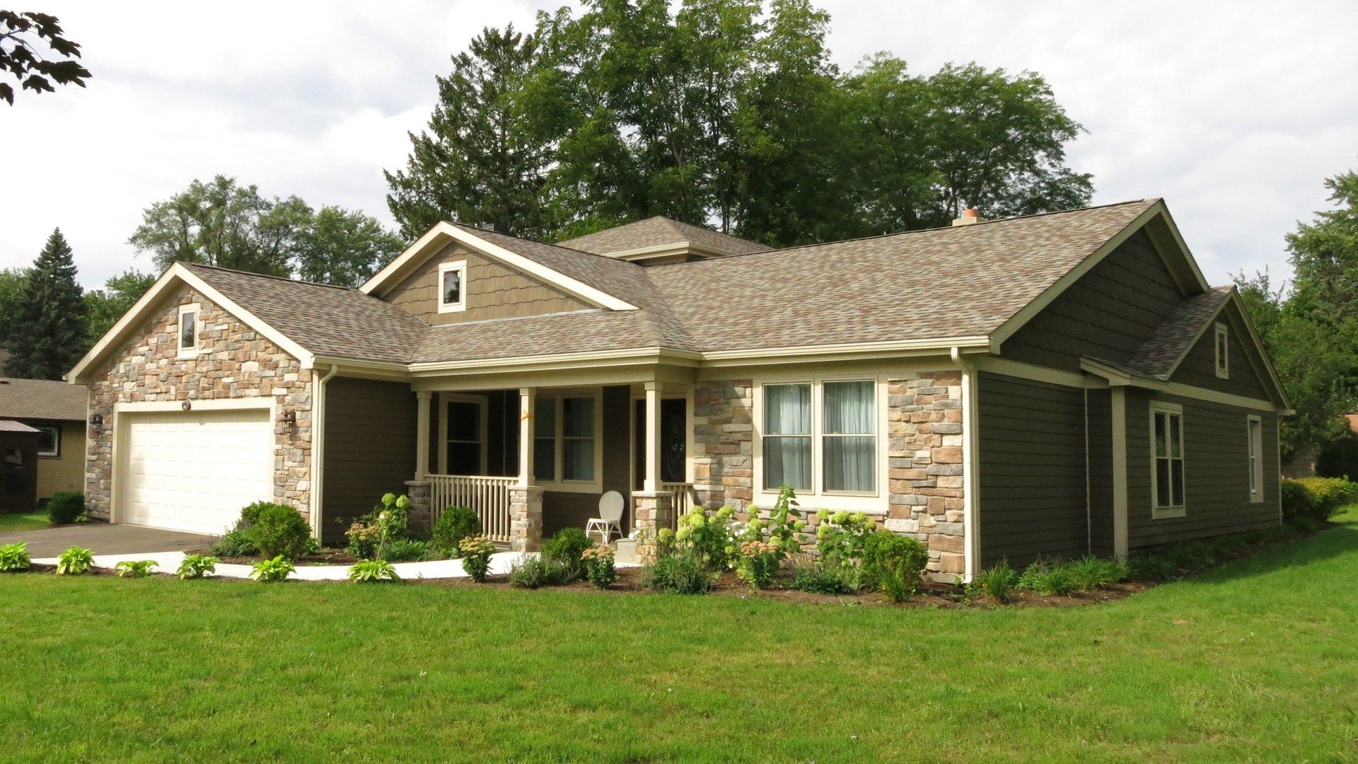 Single-story brick house with a garage, front porch, and green lawn under trees