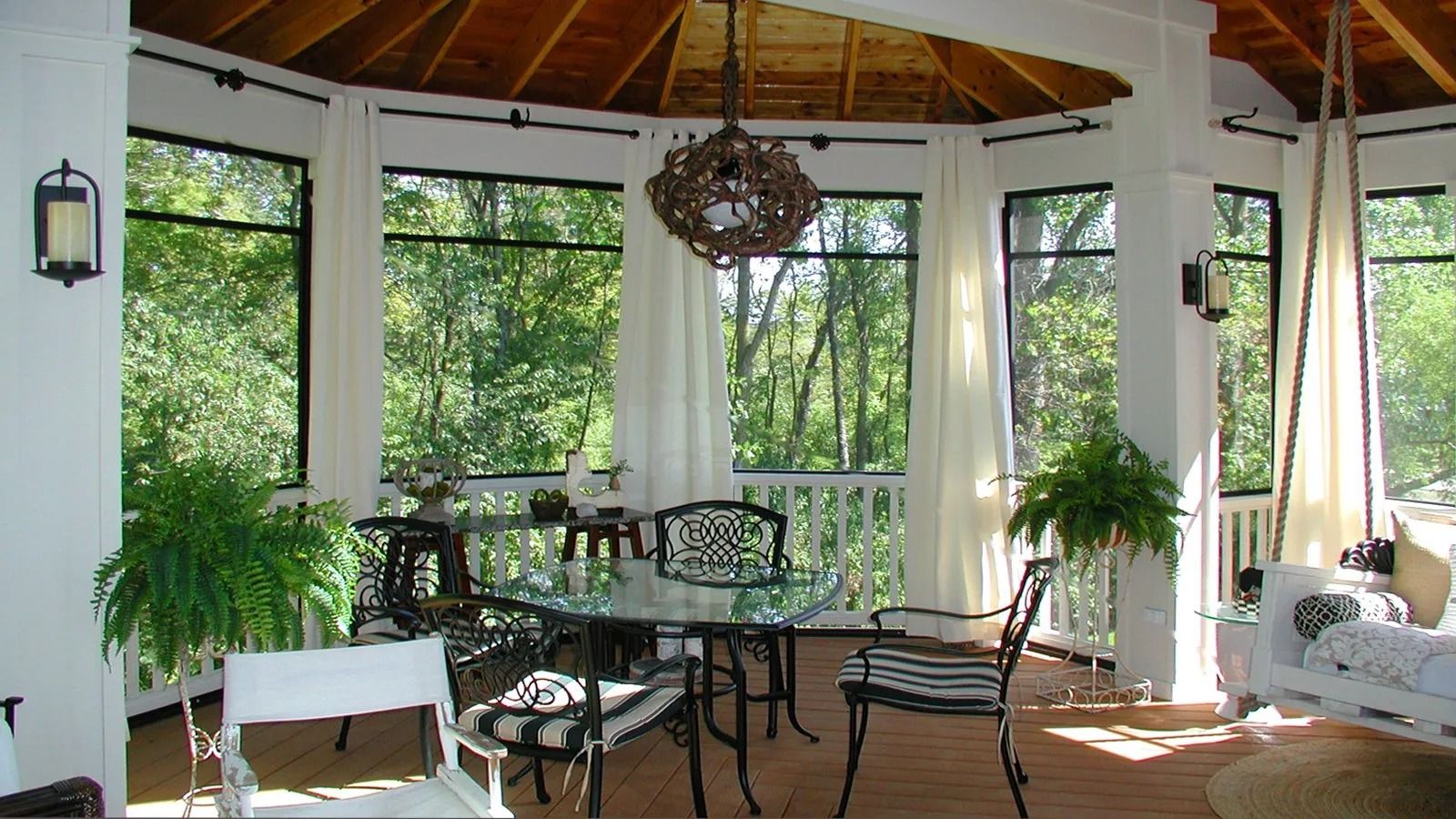 Sunroom with wicker chairs, glass table, white curtains, and potted plants in bright natural light