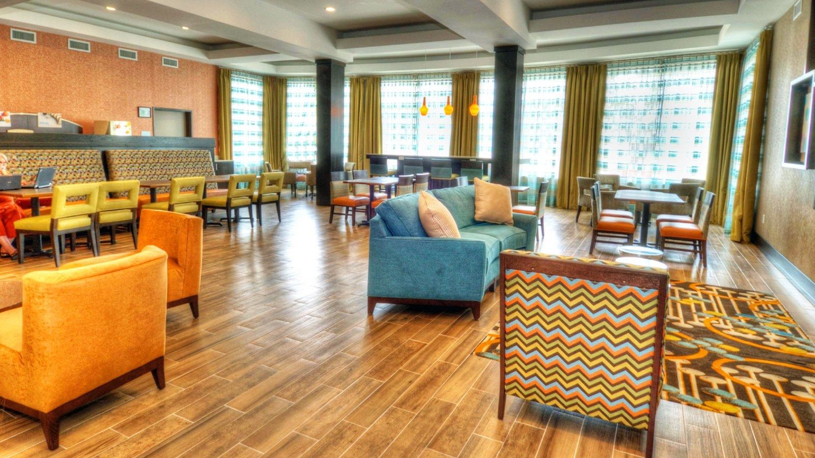Bright modern lounge with colorful chairs, sofas, wood floors, and large windows