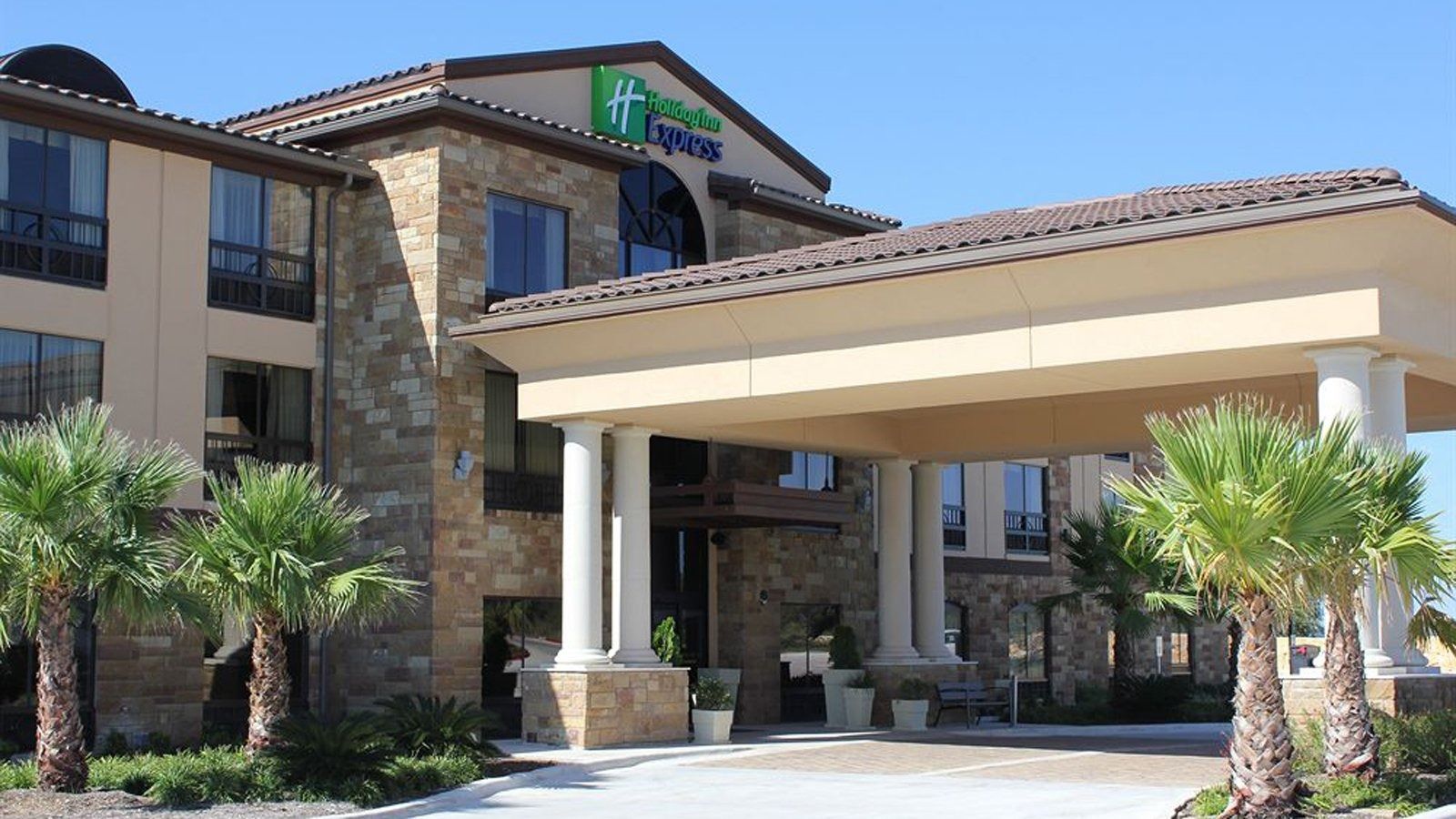 Hotel entrance with stone facade, covered driveway, and palm trees under a clear blue sky