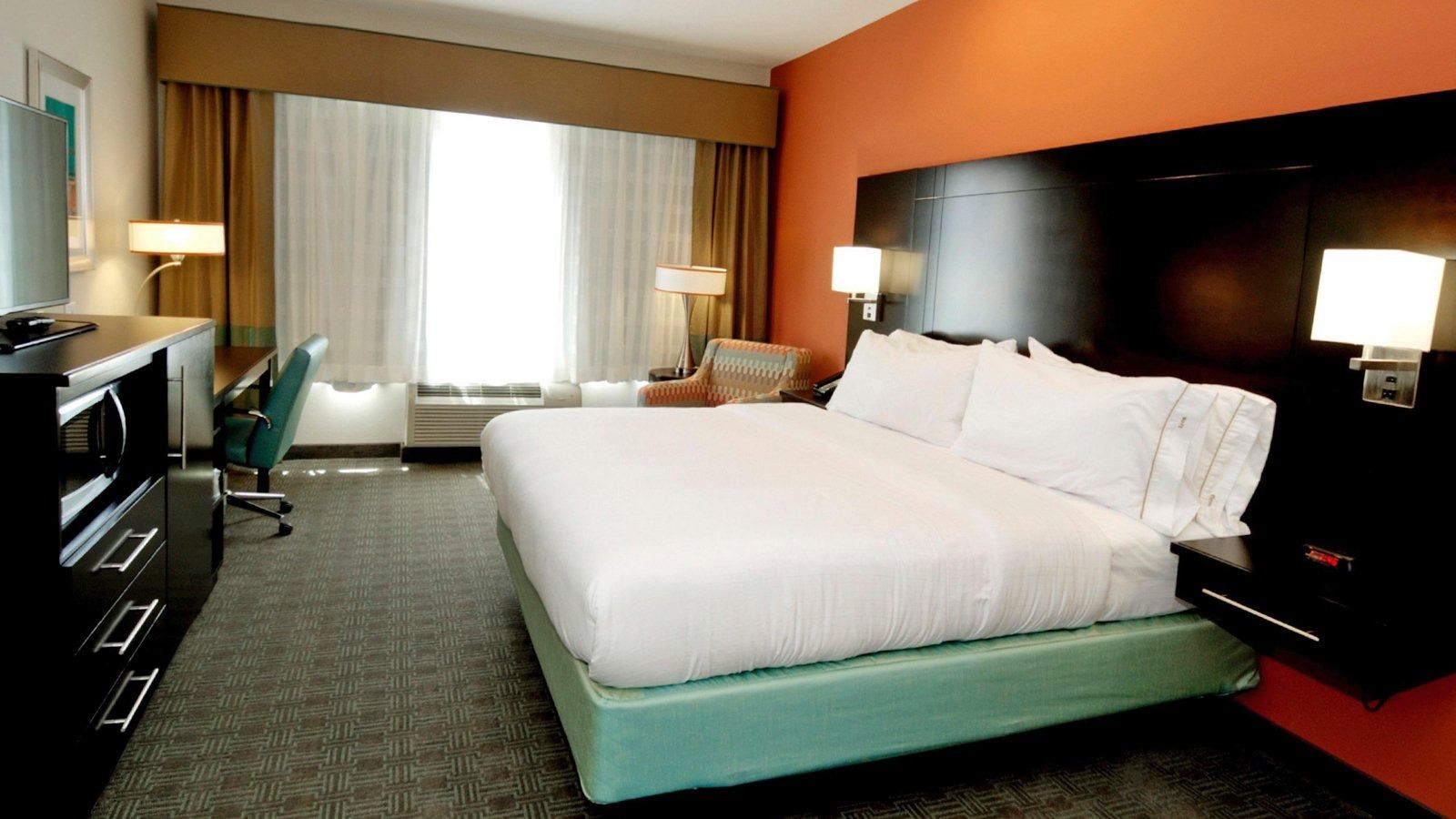 Modern hotel room with a large bed, window bench, desk, and warm lighting