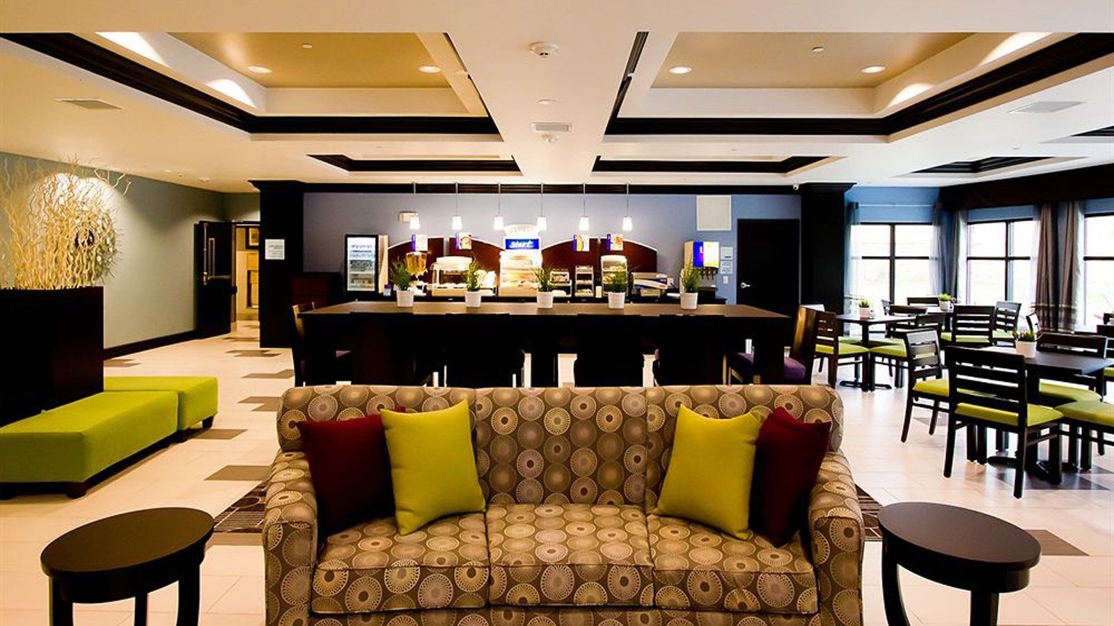 Modern hotel lobby with patterned sofa, green and red accents, bar, and dining area