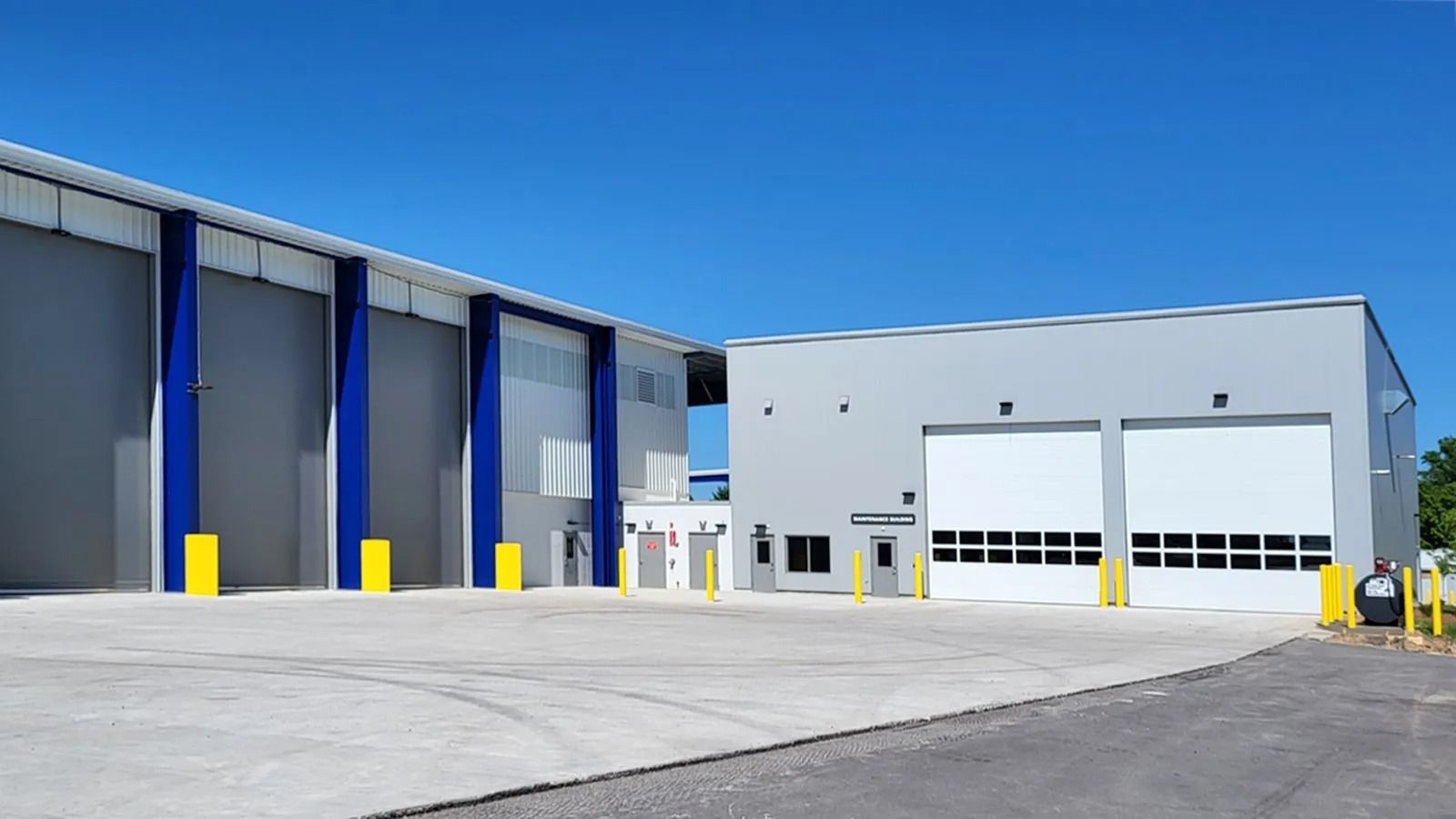 Modern industrial warehouse with blue and white exterior, large garage doors, and a paved loading area