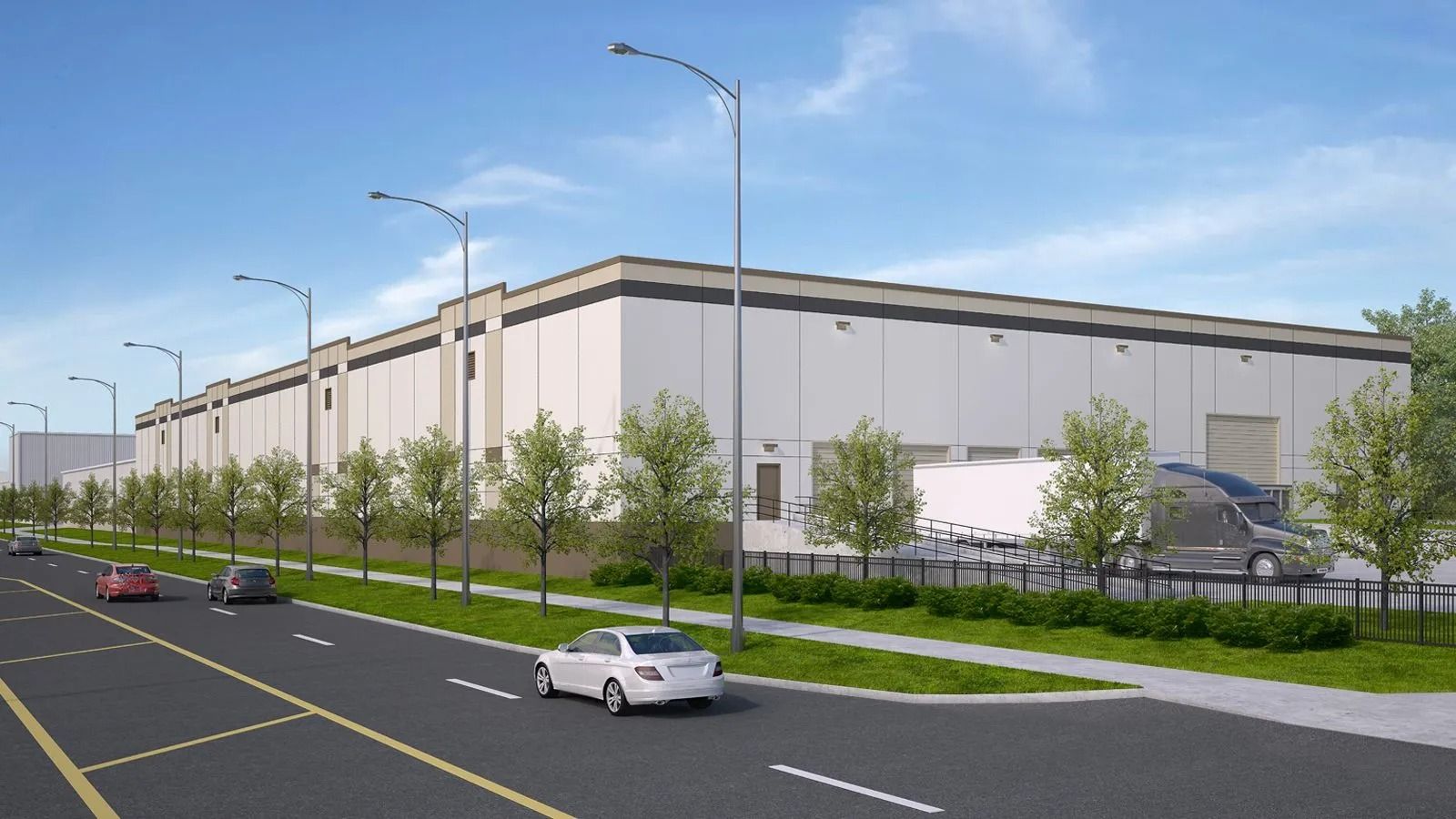 Large beige warehouse beside a road, with cars, streetlights, and young trees along the sidewalk.