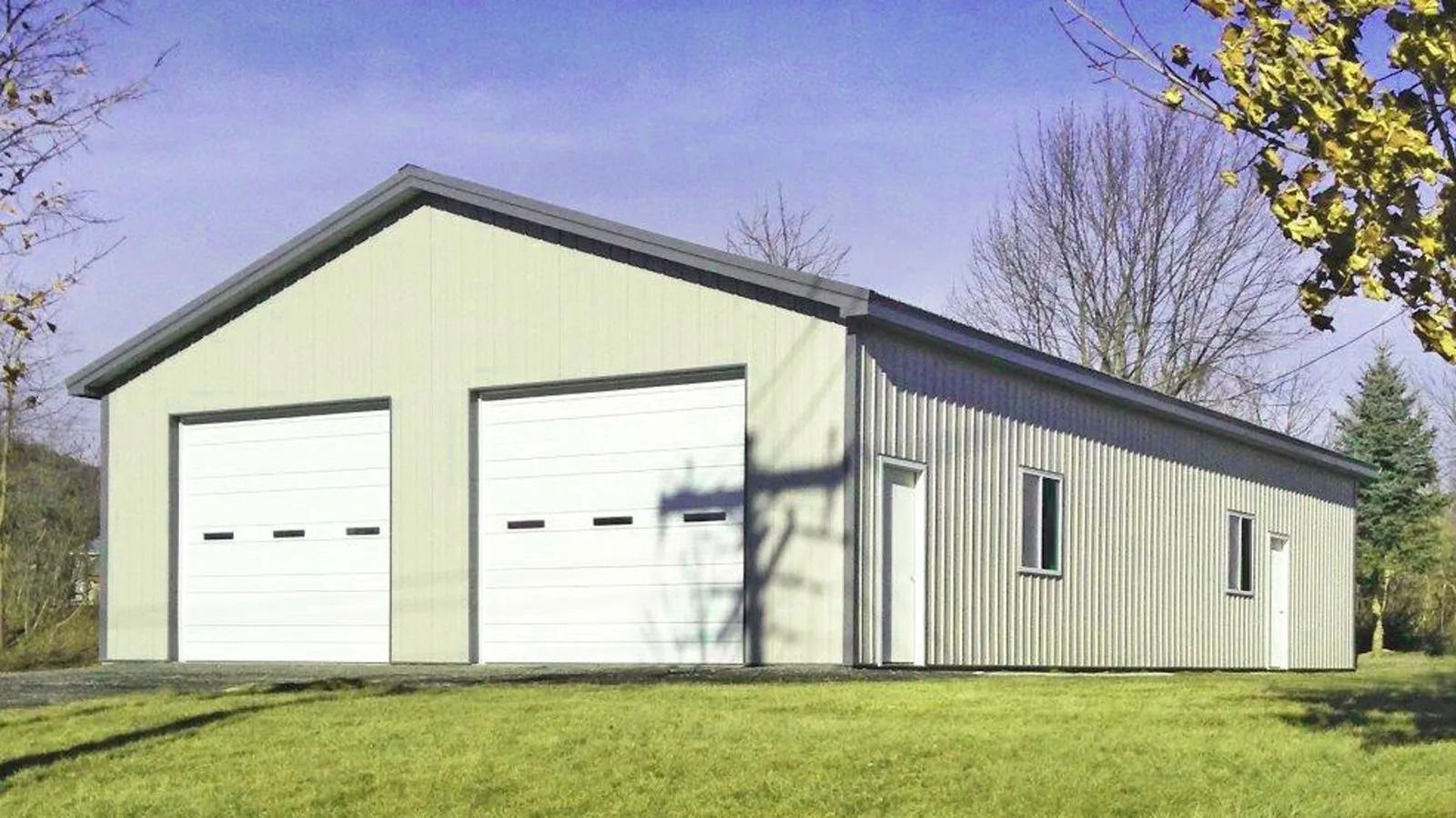 White metal garage with two large doors and a side entrance on a grassy lot under a clear sky
