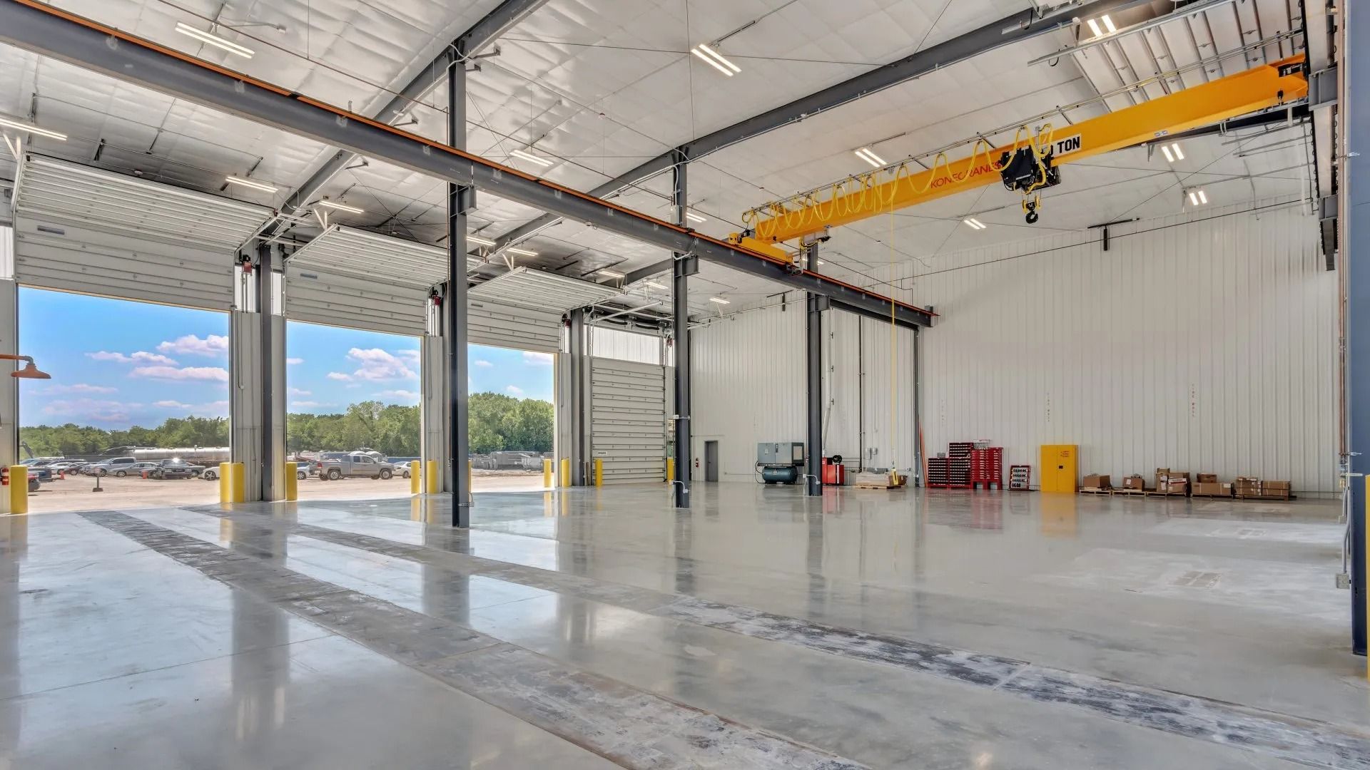 Empty industrial warehouse with polished concrete floor, steel beams, and overhead yellow crane rail
