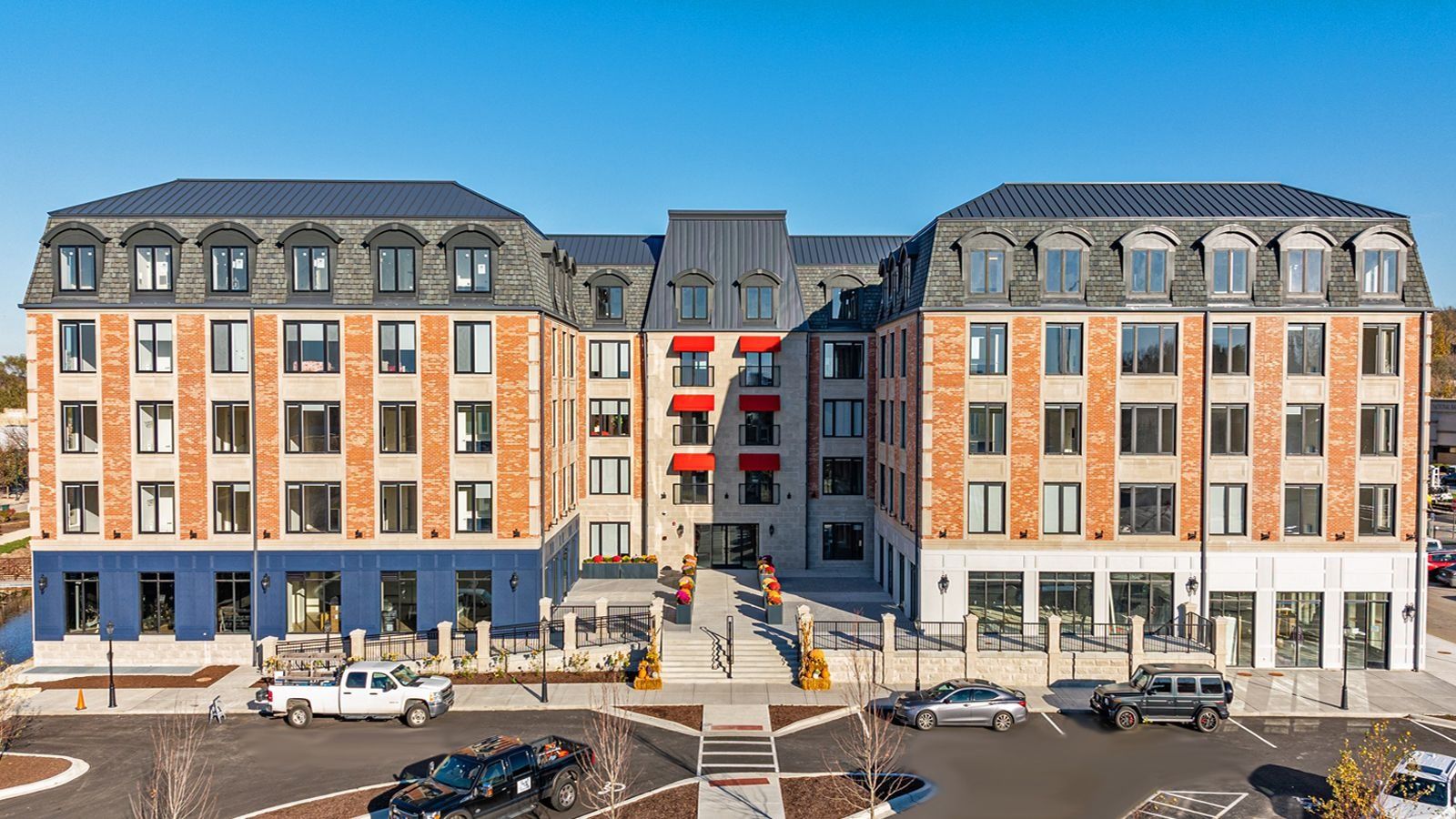 Modern apartment building with orange and blue facades, central red balconies, and parked cars outside