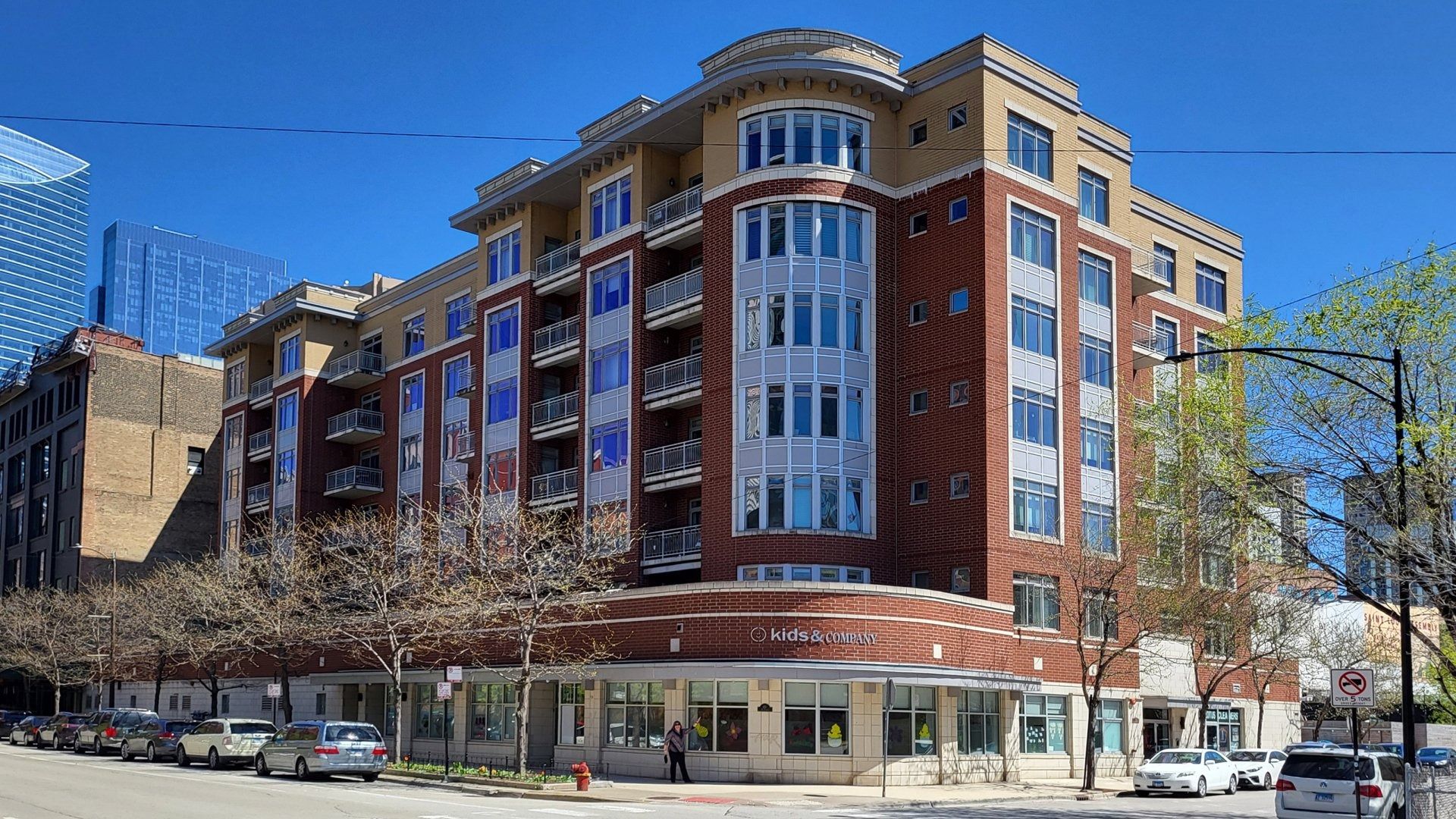 Corner brick apartment building with large windows and storefronts on a sunny city street