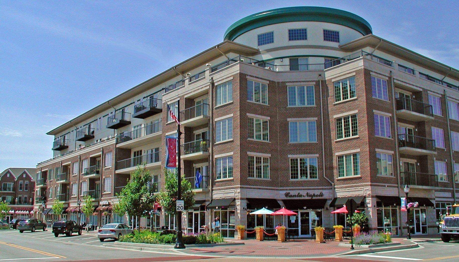 Street corner with a multi-story brick apartment building, shops at ground level, and a circular rooftop tower.