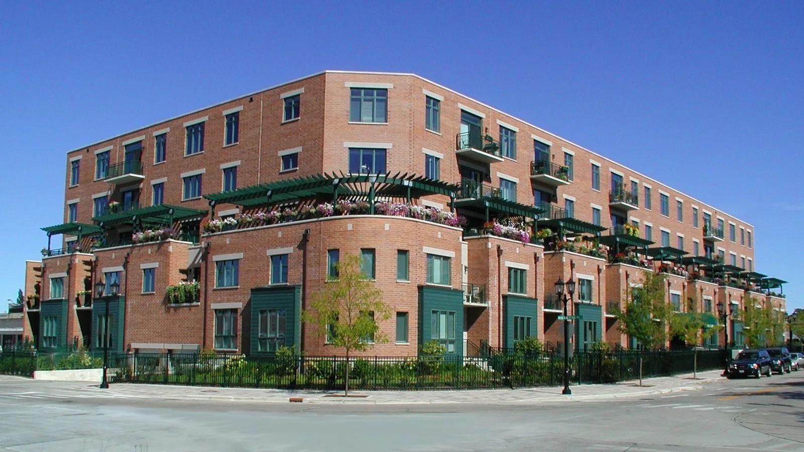 Large brick apartment building with green balconies on a street corner under a clear sky