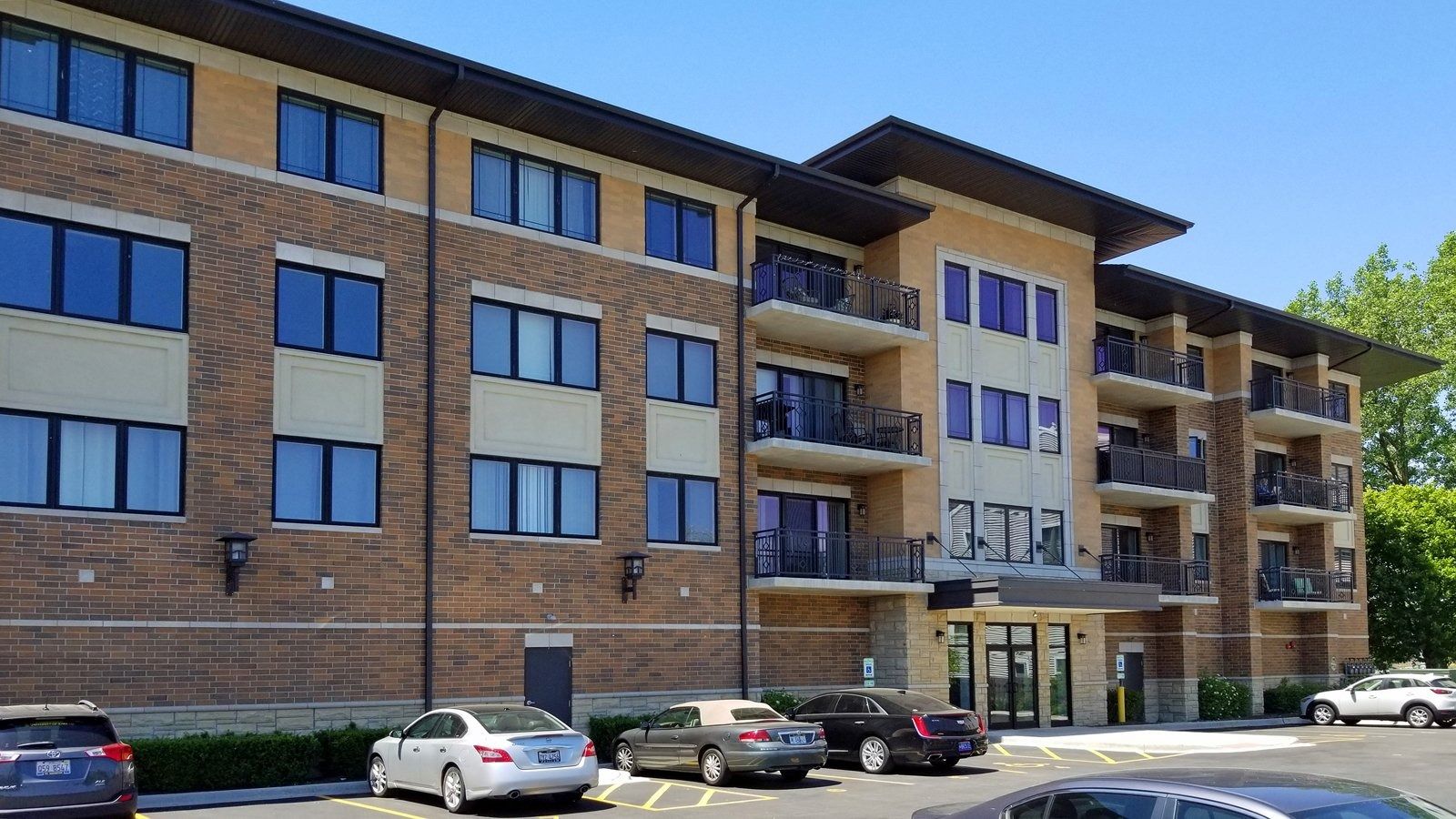 Modern brick apartment building with balconies and parked cars in front