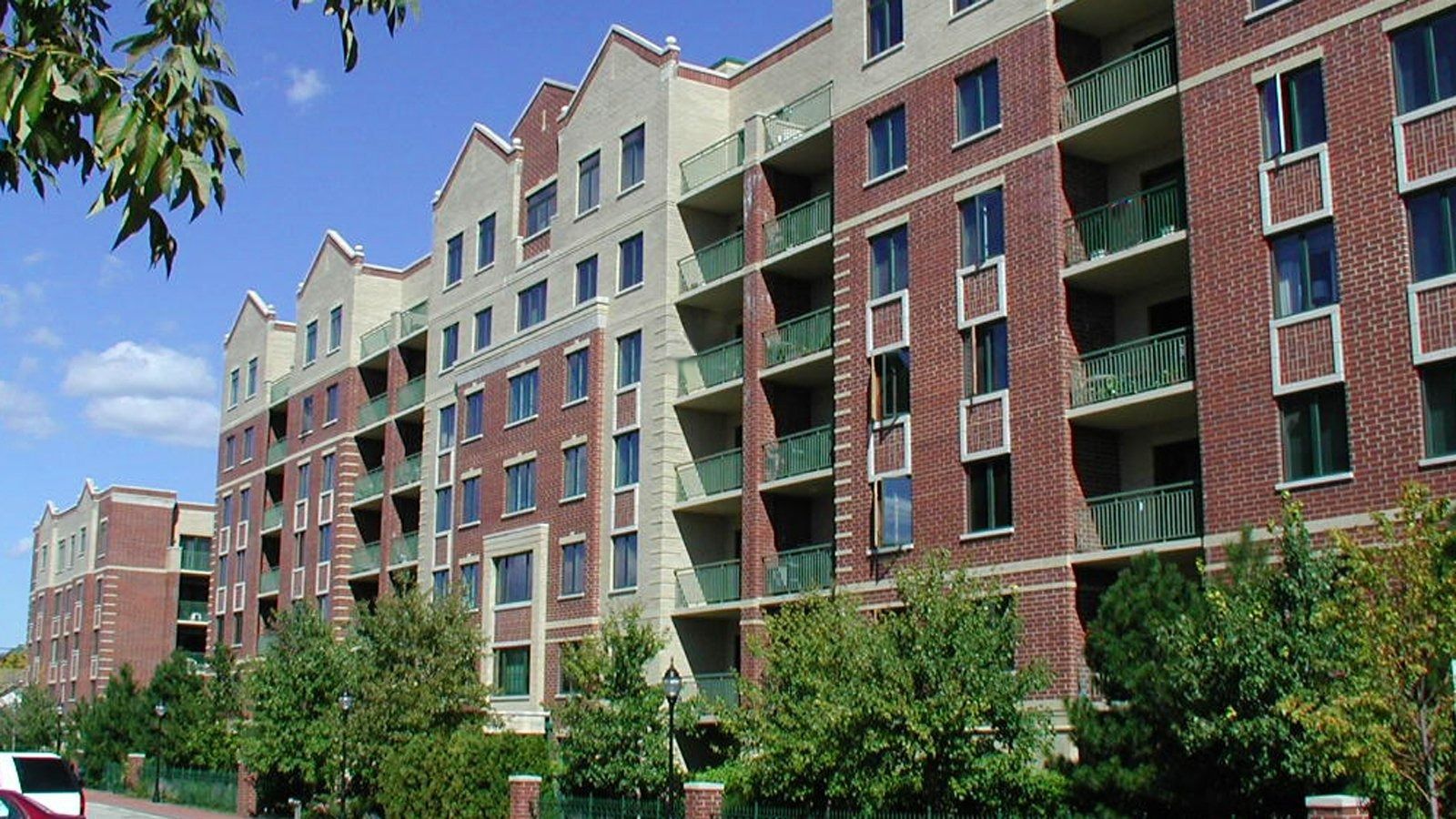 Colorful brick apartment buildings with balconies along a tree-lined street under a clear blue sky