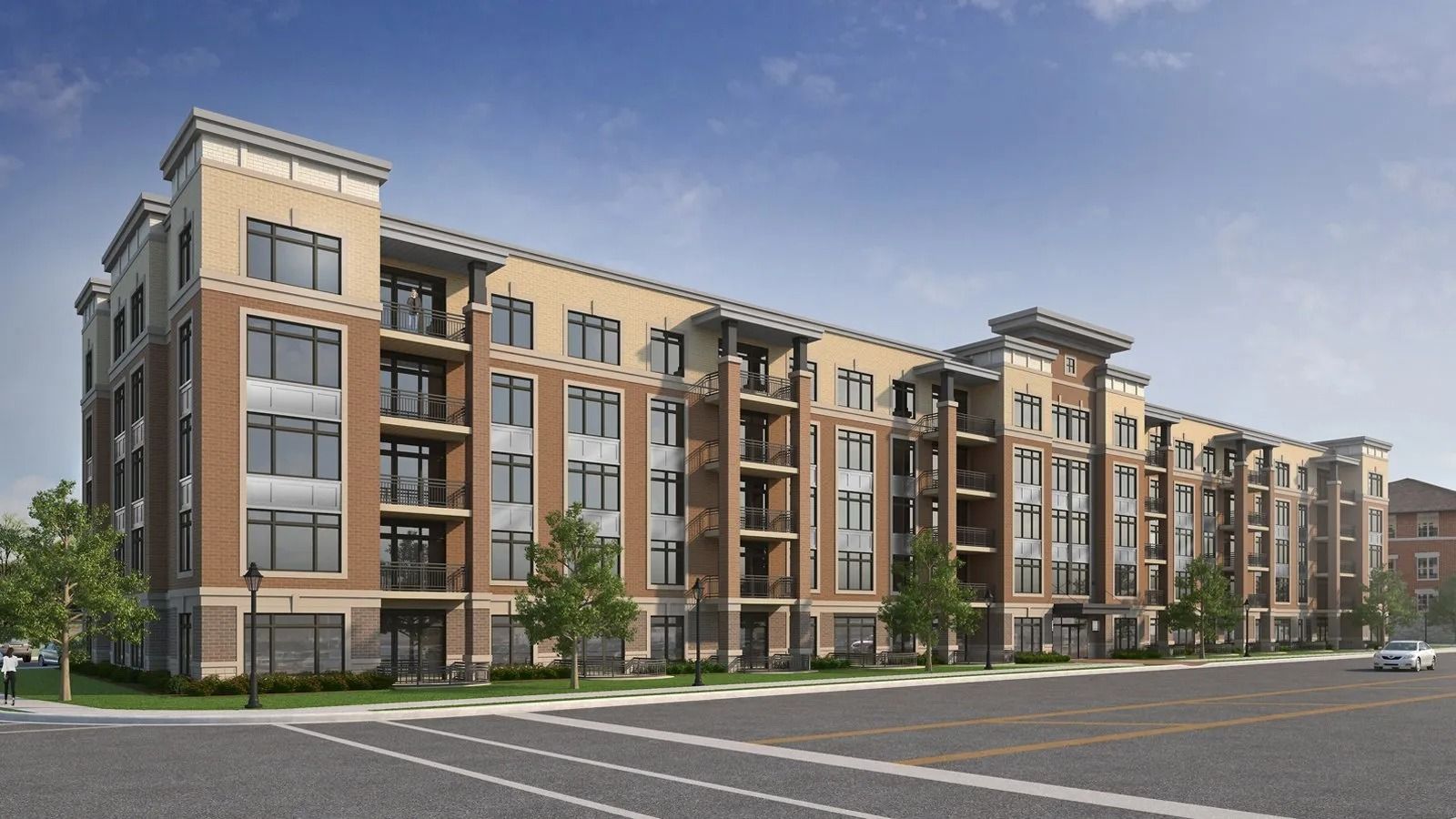 Modern multi-story apartment building with tan and gray exterior beside a wide parking lot under a blue sky