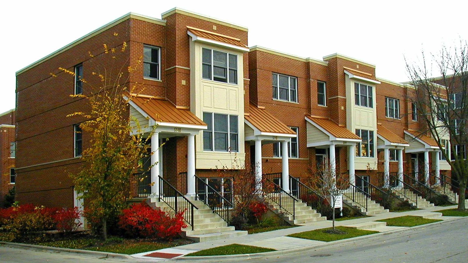 Row of brick townhouses with small porches along a quiet residential street