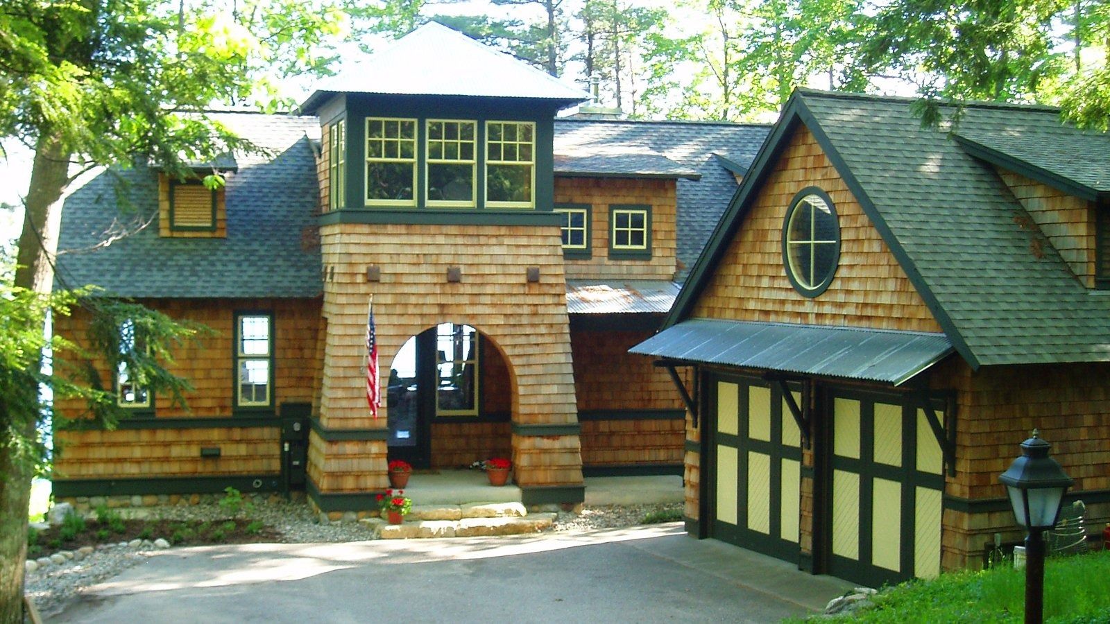 Wooded lodge with stone archway and Tudor-style buildings, including a turreted entrance and sloped roofs