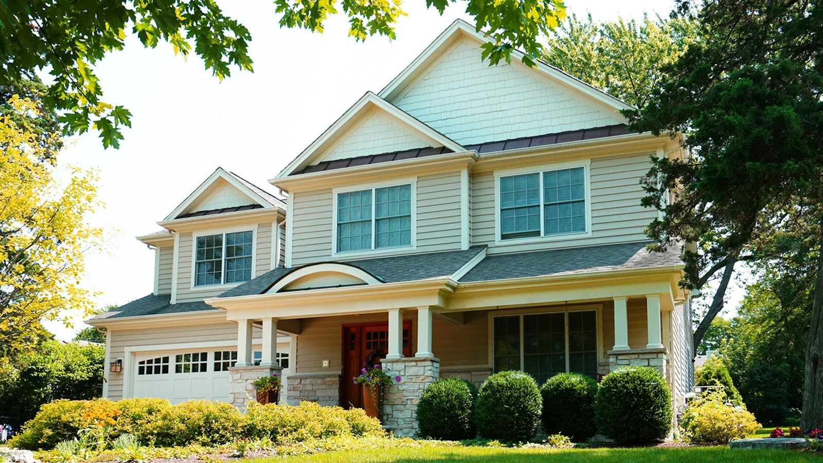 Large white two-story house with a front porch, shutters, and manicured lawn in bright sunlight
