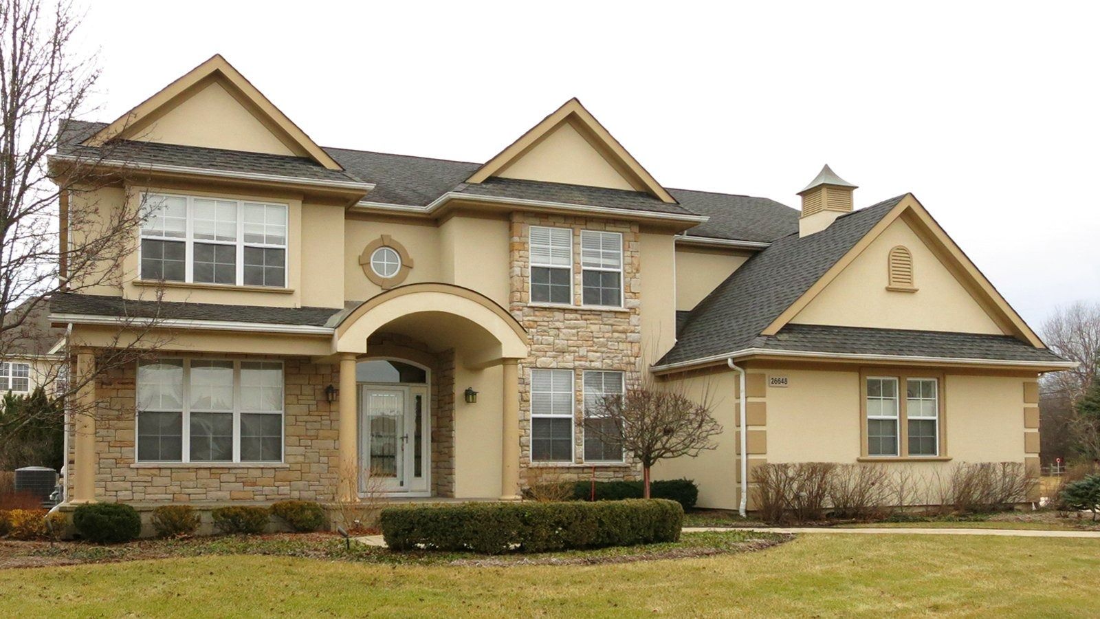 Large two-story stone house with beige siding, a dark roof, and a front lawn