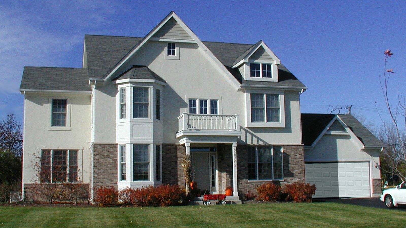Large gray two-story suburban house with white trim, front porch, and attached garage on a sunny day