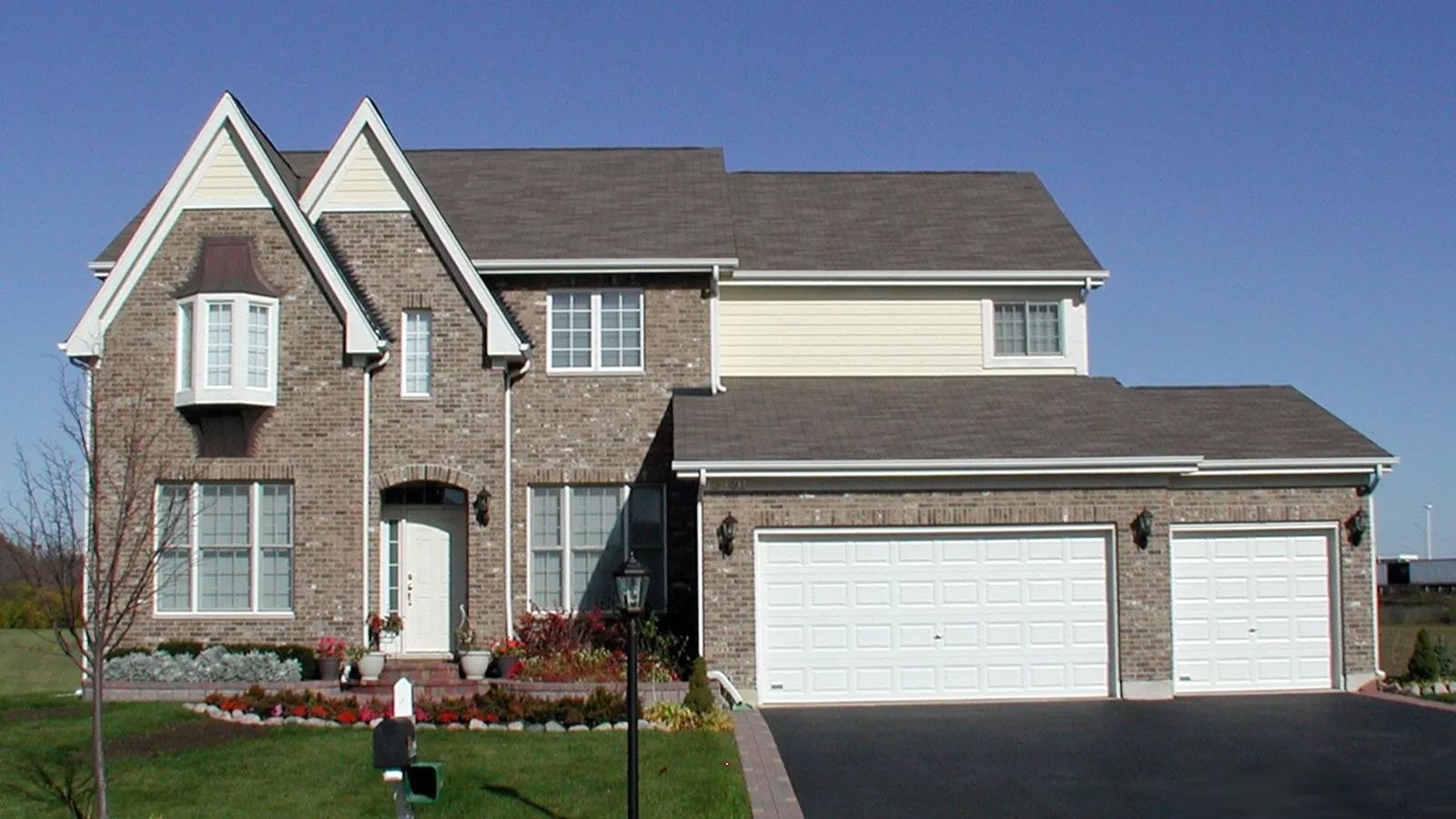 Suburban two-story brick house with a three-car garage and front lawn, viewed from the street