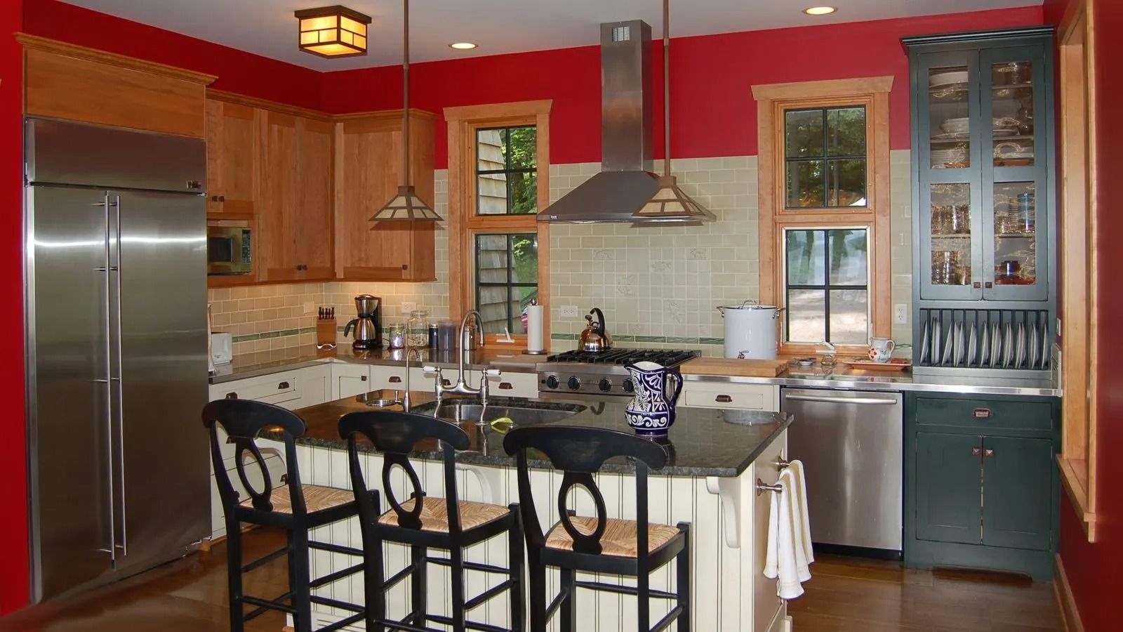 Modern kitchen with red walls, wood cabinets, stainless appliances, and a central island with bar stools