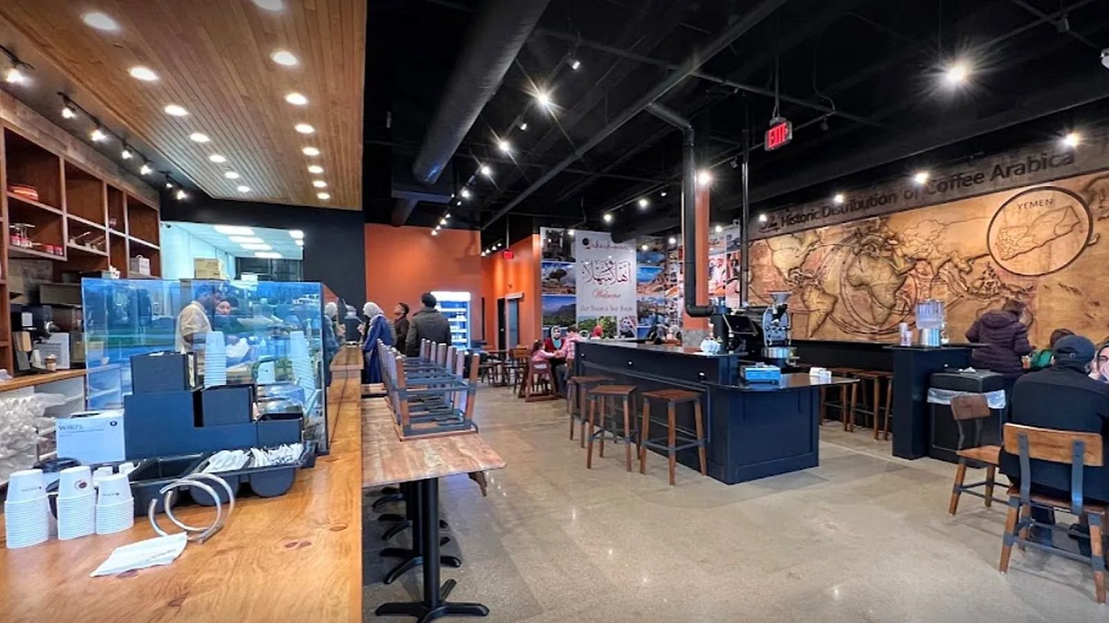 Modern cafe interior with wooden floors, black tables, bar seating, and warm pendant lighting