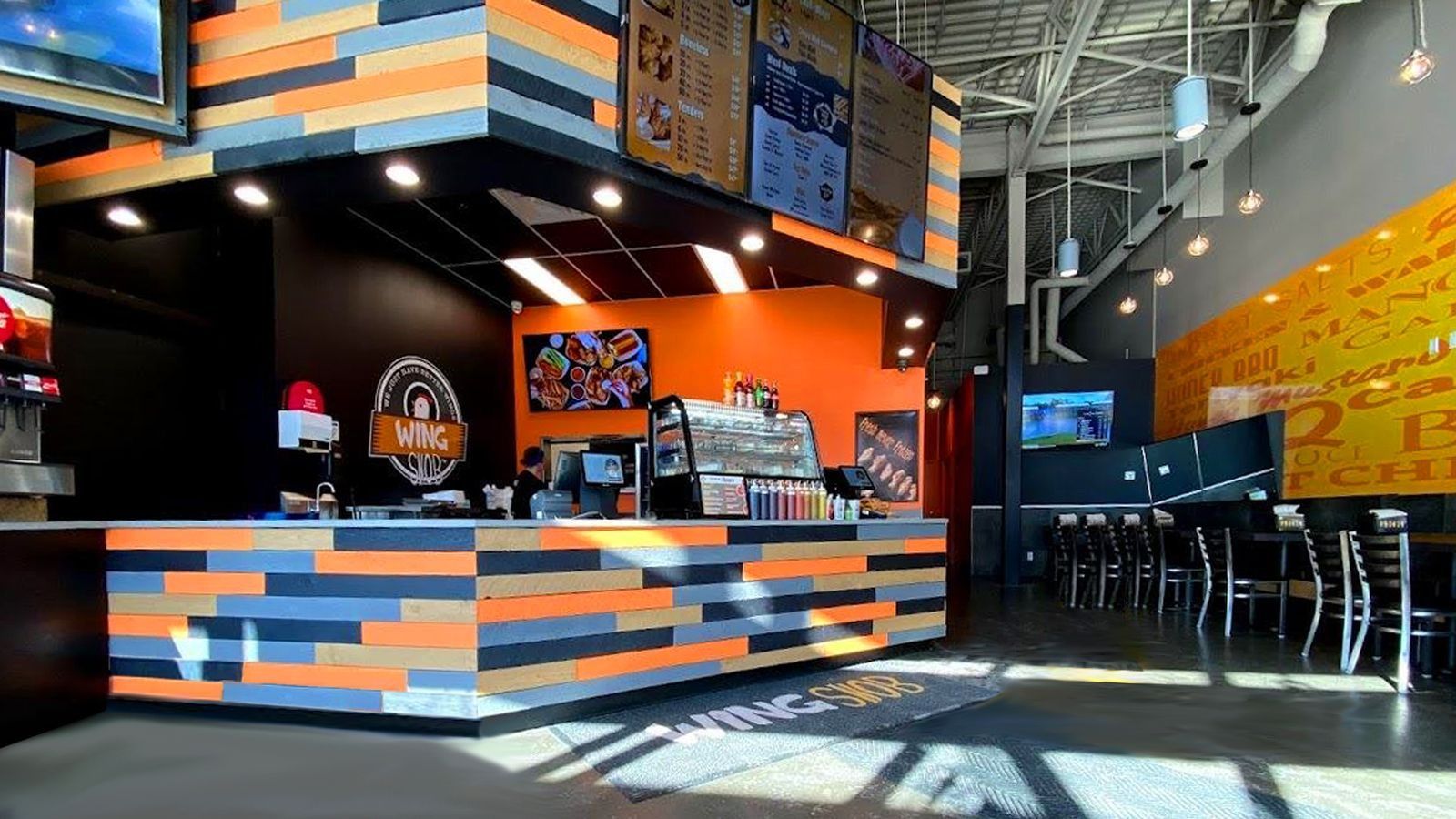 Modern café interior with orange-and-gray counter, hanging menu boards, and seating area by large windows