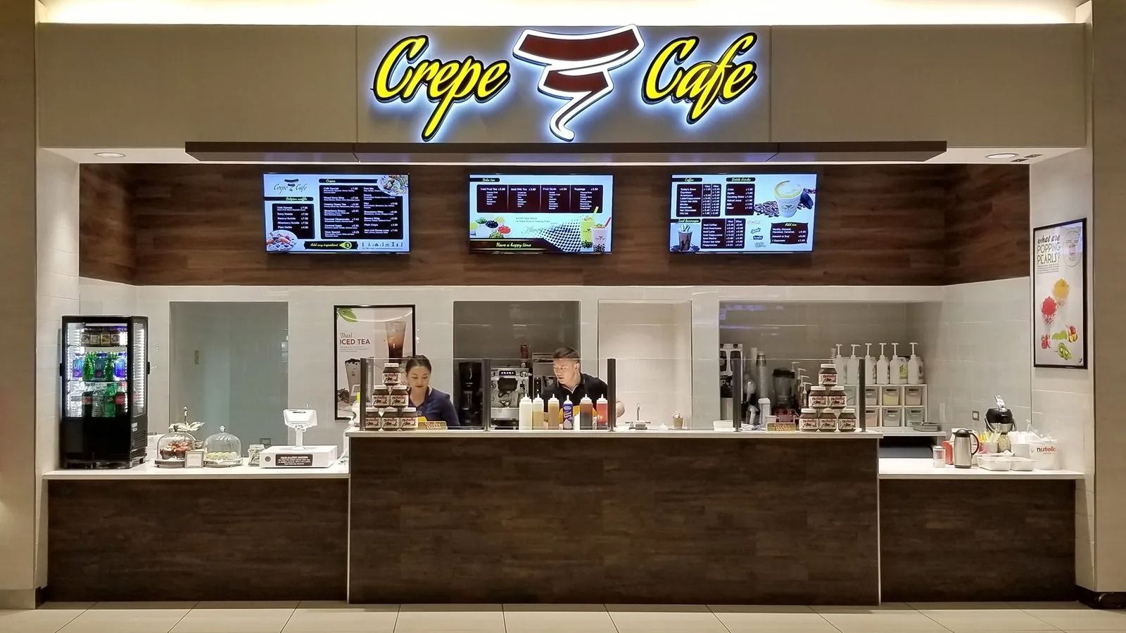 Crêpe Cafe counter with menu screens, glass display, and dark wood front in a bright mall kiosk