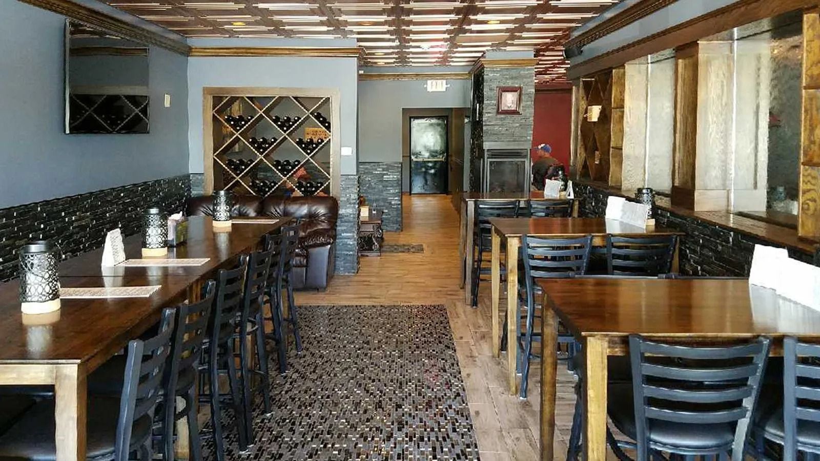 Empty restaurant dining room with wooden tables, black chairs, and a patterned rug