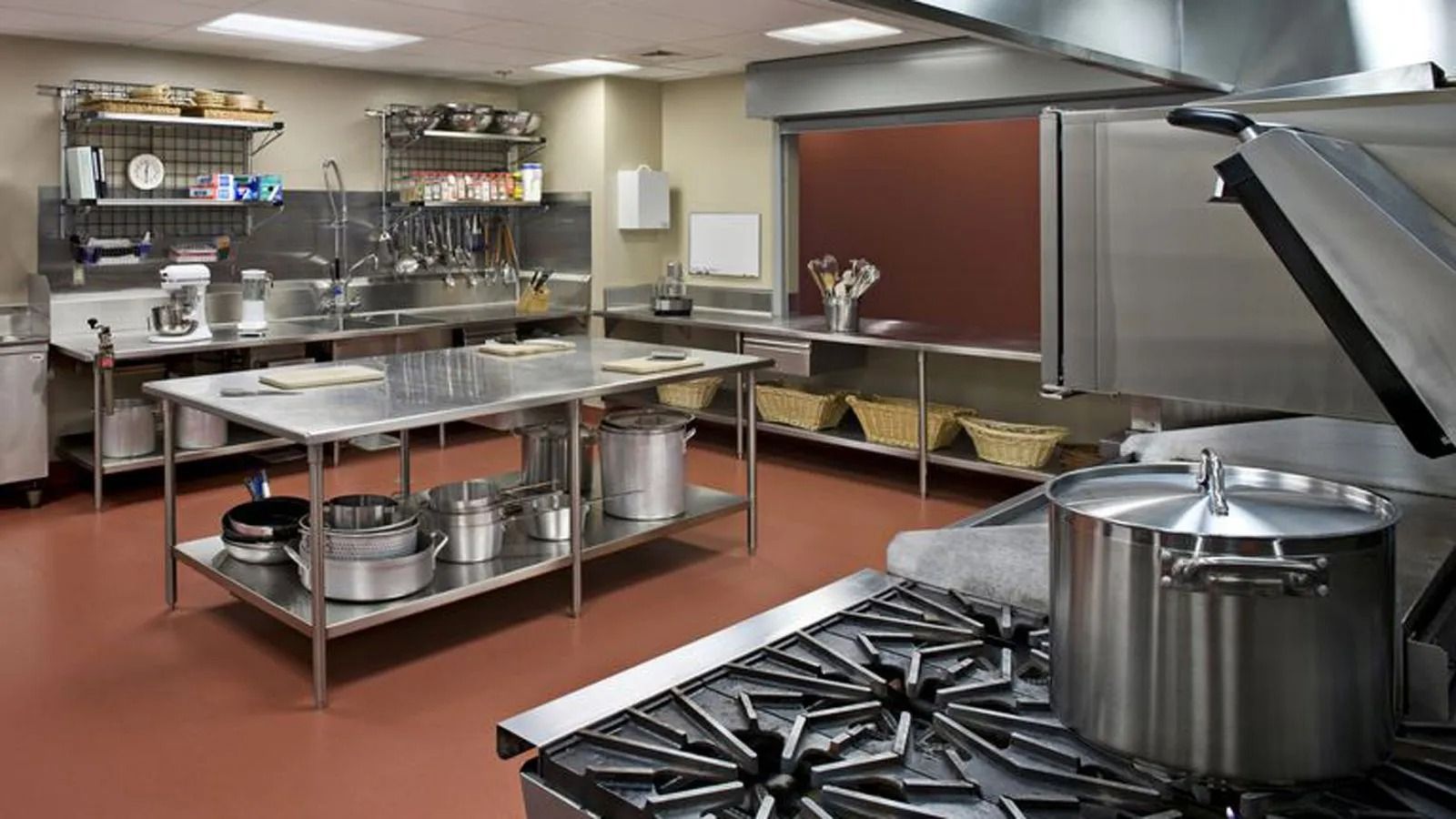 Commercial kitchen with stainless steel counters, pots, and large stove under bright overhead lights