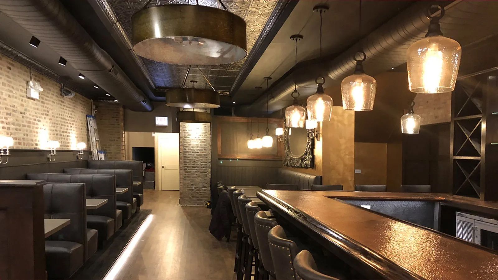 Empty modern restaurant bar with booths, pendant lights, brick walls, and a polished wooden counter