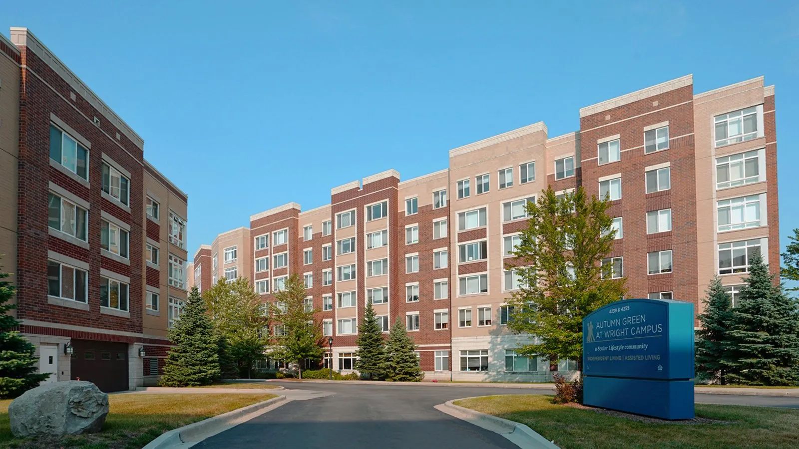Modern brick apartment buildings along a driveway with a blue sign under a clear sky