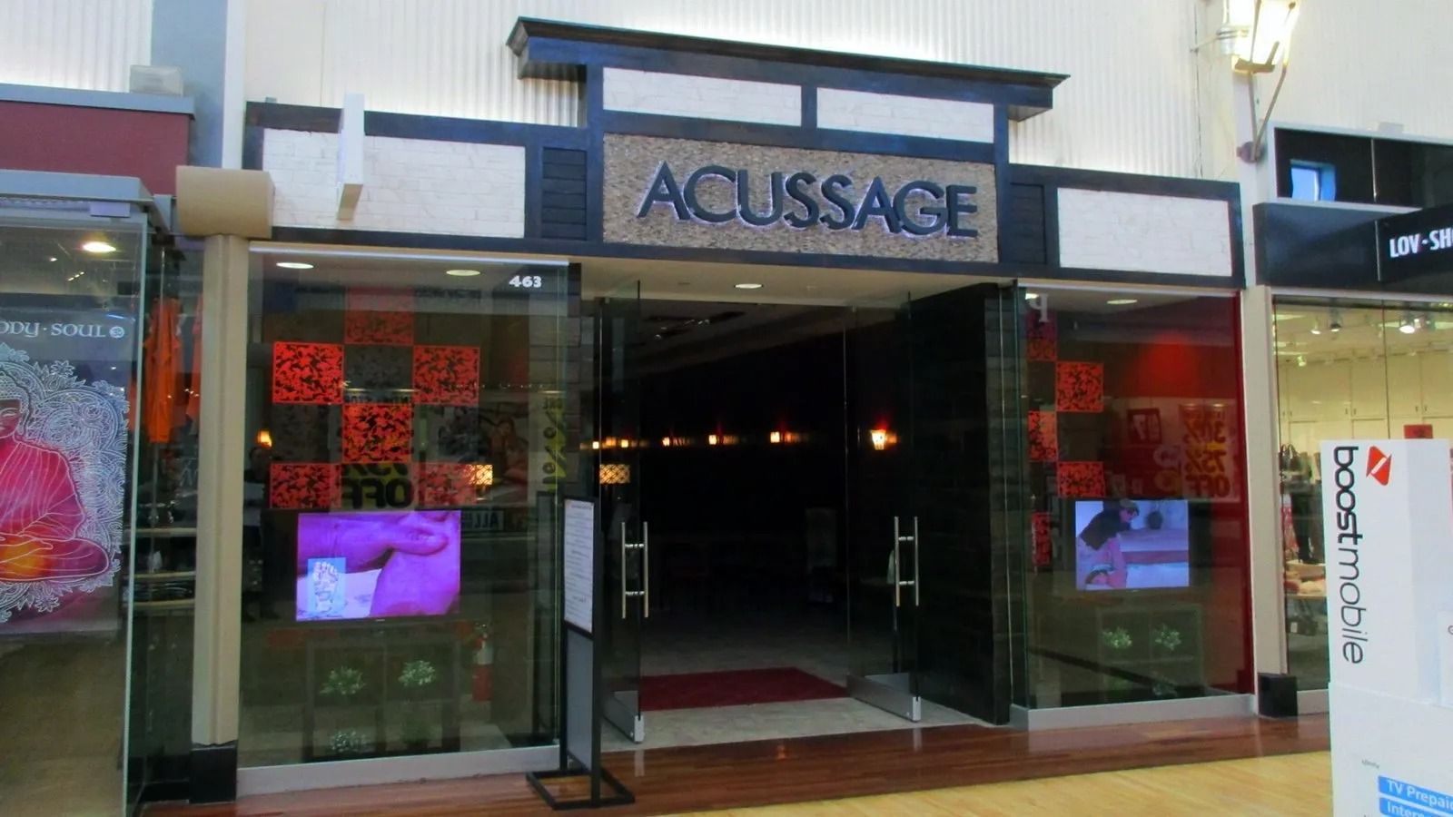 Storefront entrance with “ACUSSAGE” sign and illuminated display screens at dusk.