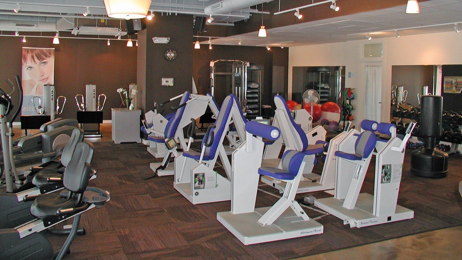 Gym interior with rows of white exercise machines and treadmills under bright ceiling lights.