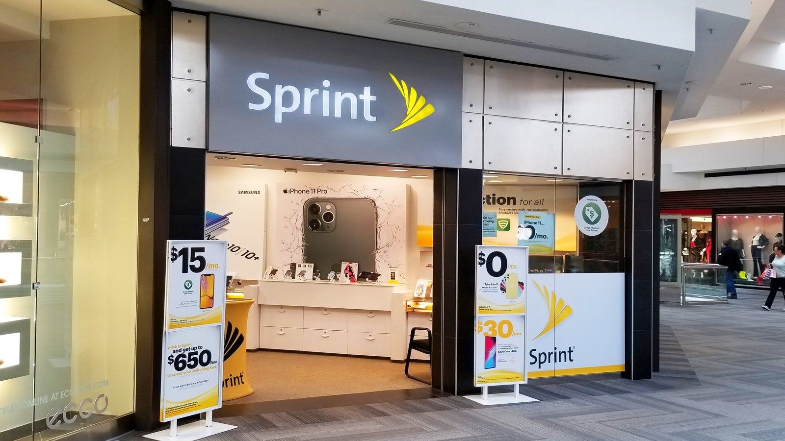 Sprint store entrance in a mall, with bright gray and yellow signage and glass doors.