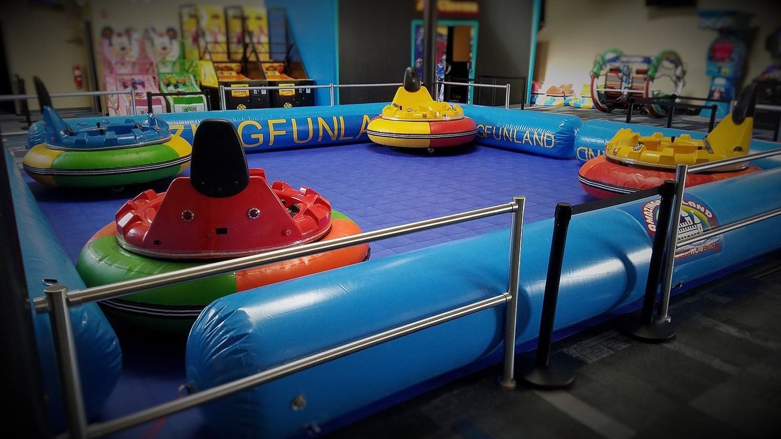 Colorful bumper car arena with blue padded barriers and several empty red, yellow, and green cars