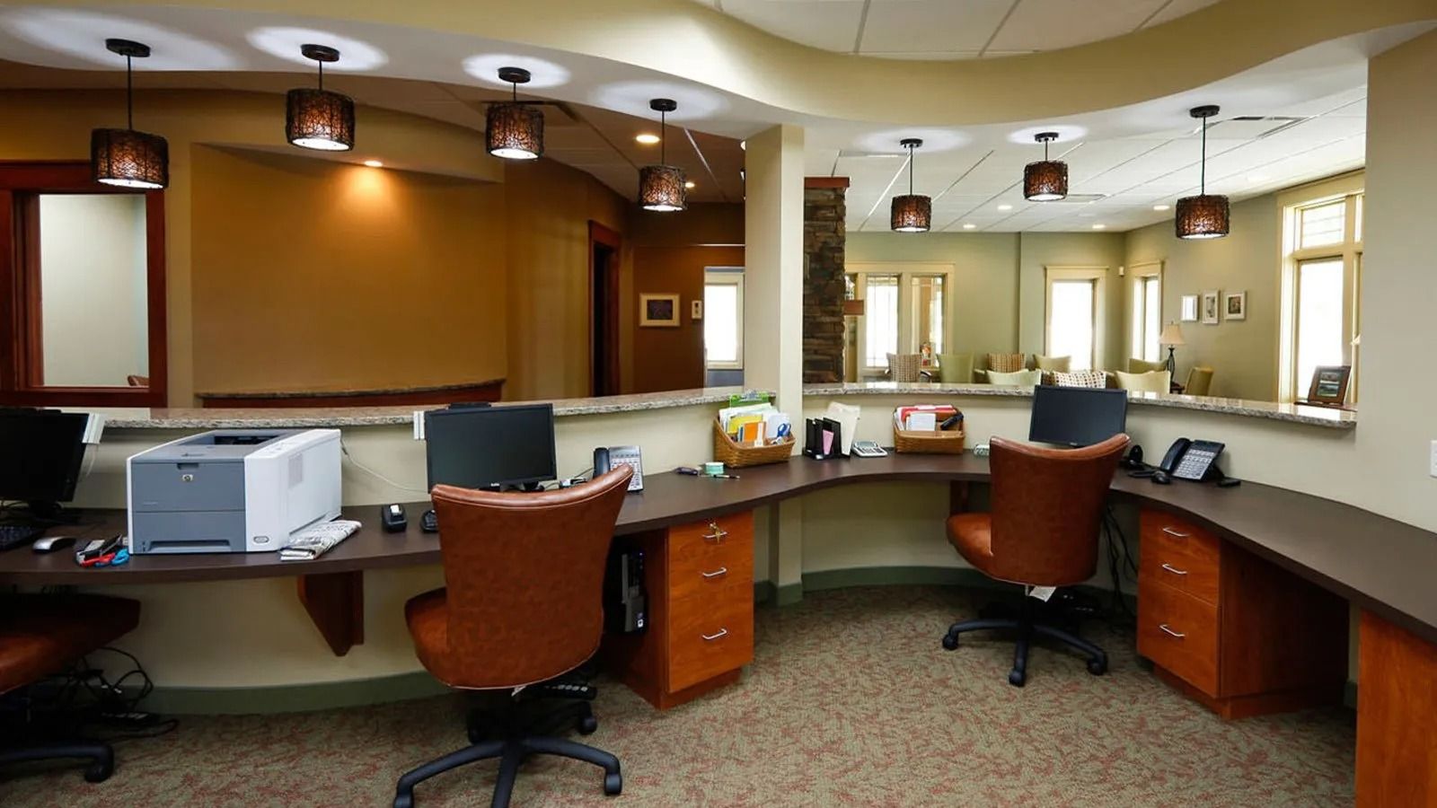 Empty reception desk area with brown chairs, computer monitors, and warm ceiling lights