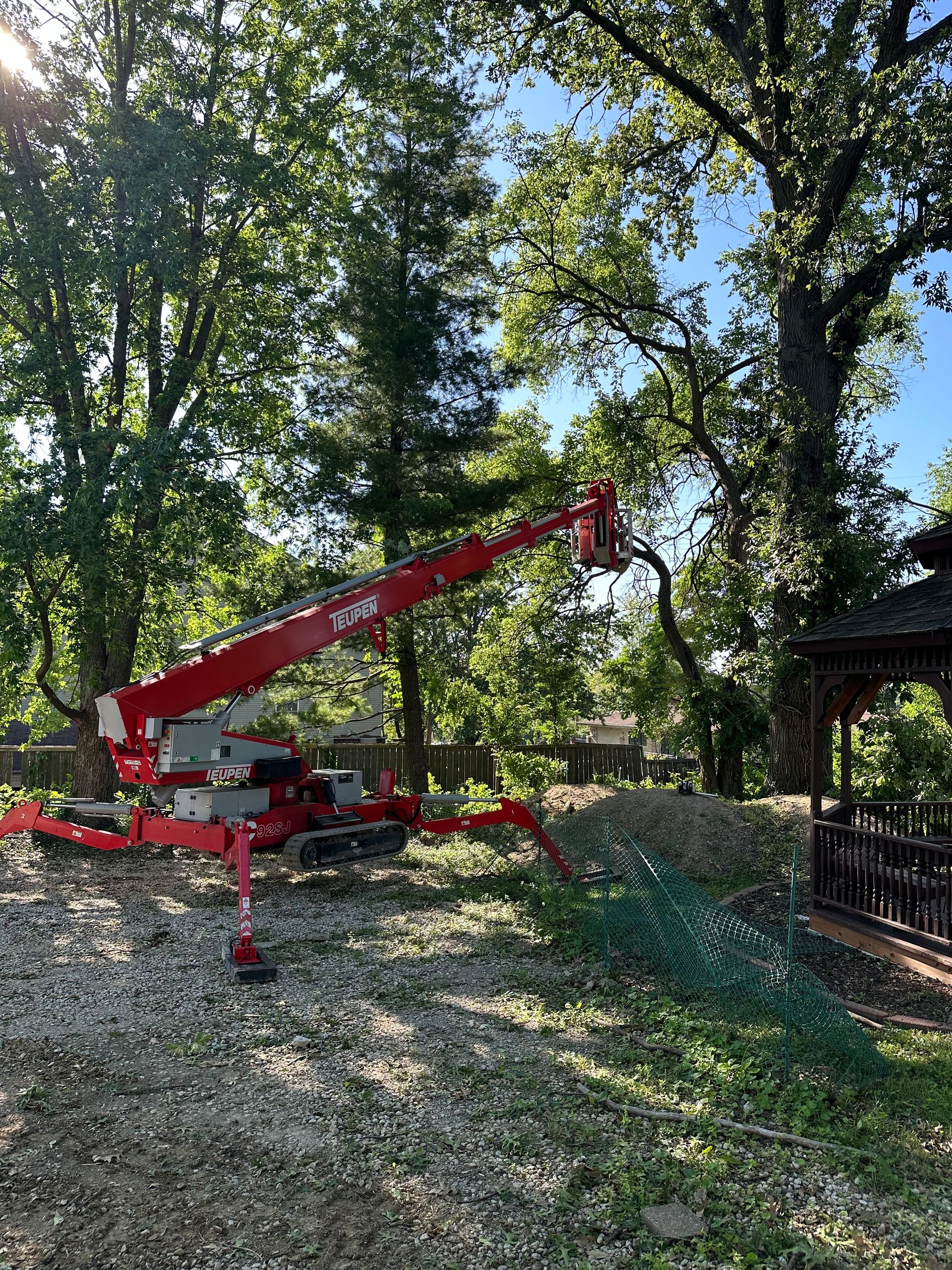 A red crane is cutting a tree in a yard.