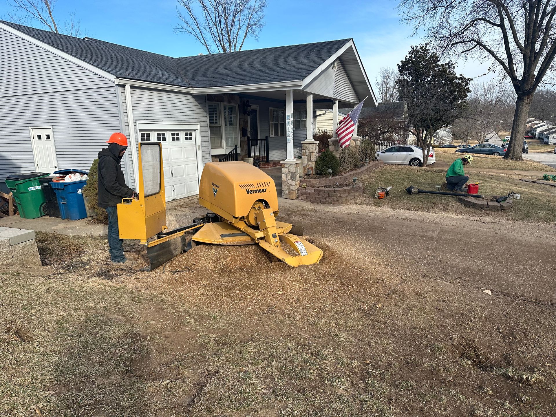A man is working on a stump grinder in front of a house.
