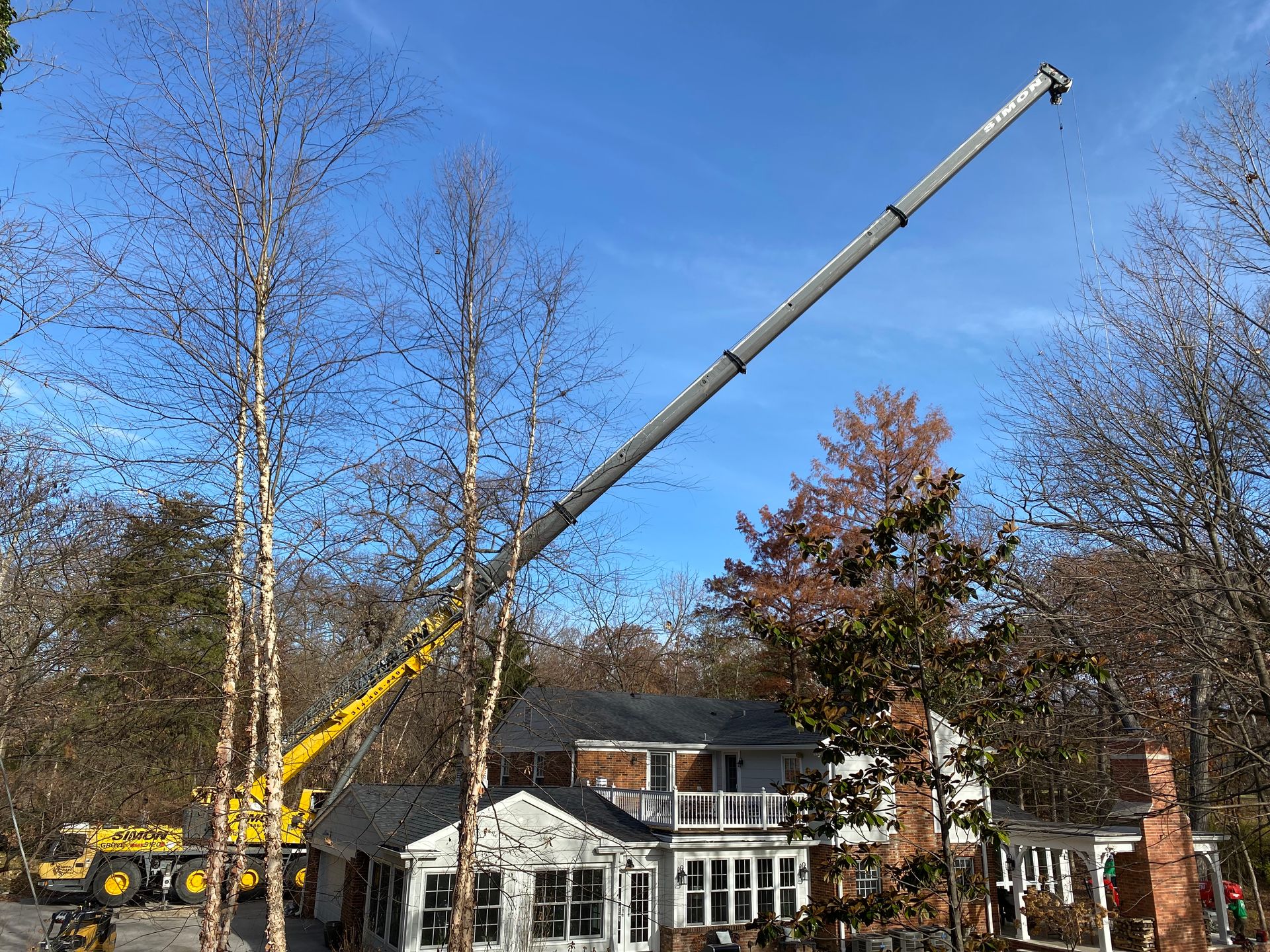A large crane is lifting a tree in front of a house.
