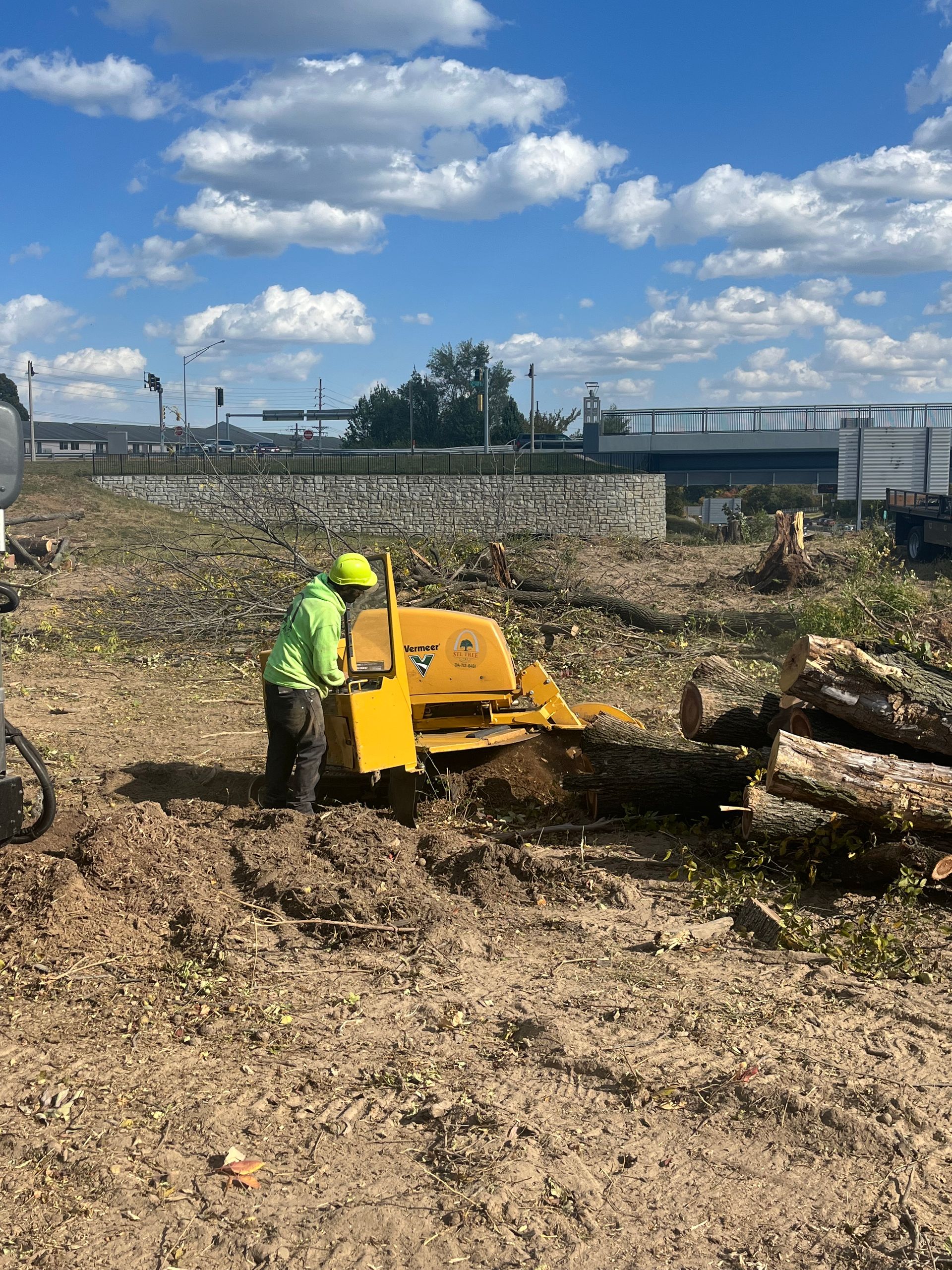 A man is using a machine to remove a tree stump in a field.