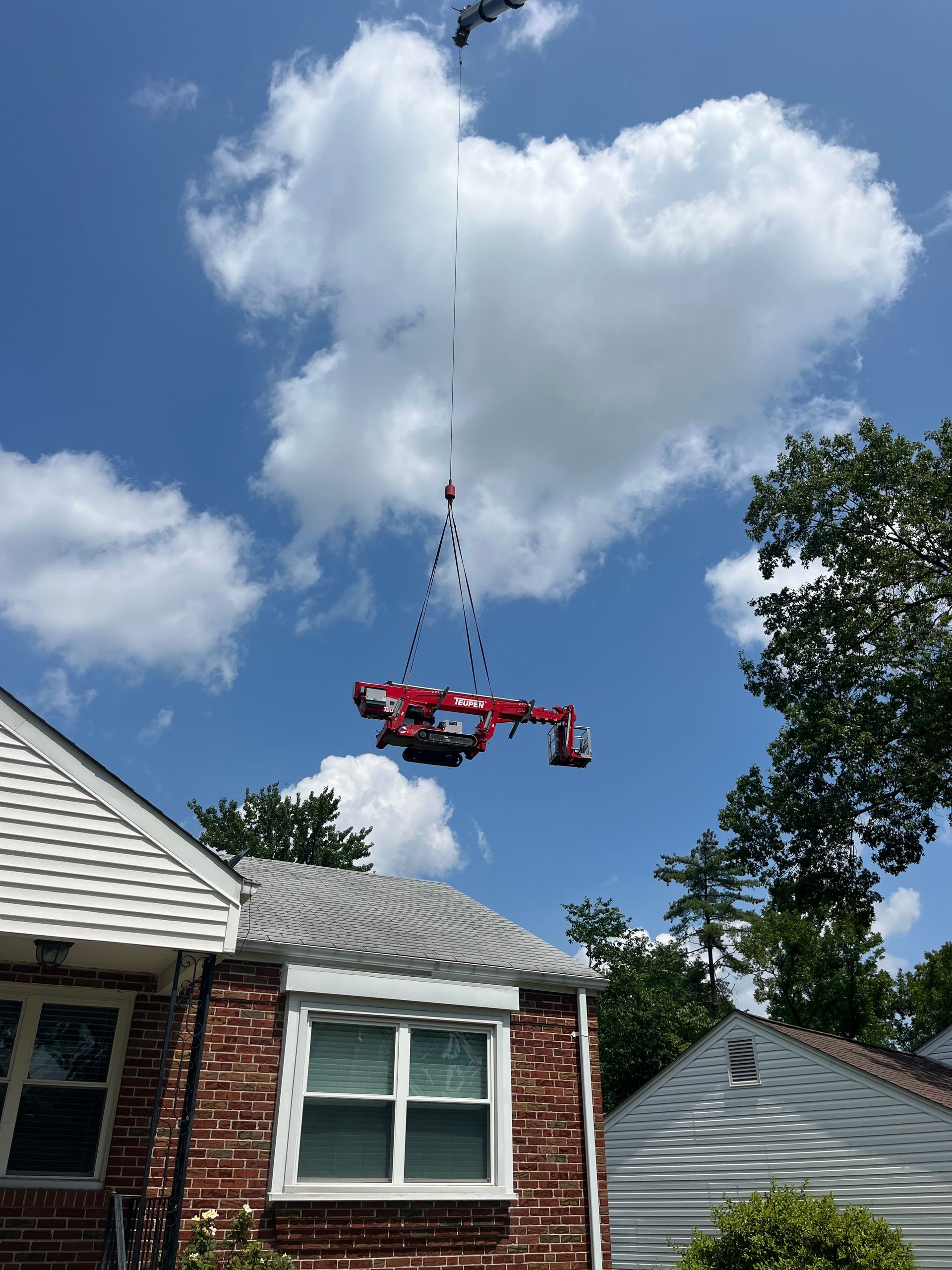 A red crane is lifting a brick house in the air