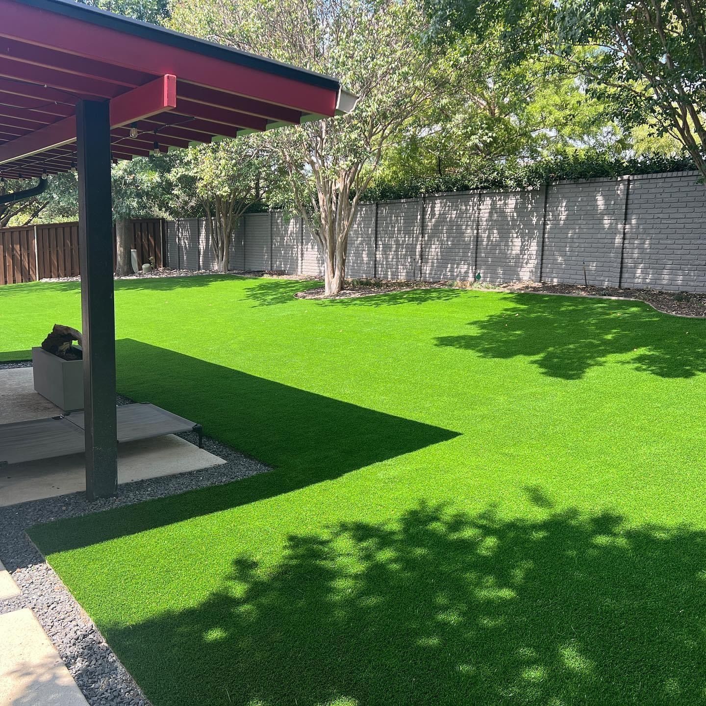 Backyard with bright green lawn, patio cover, trees, and a stone fence in sunlight