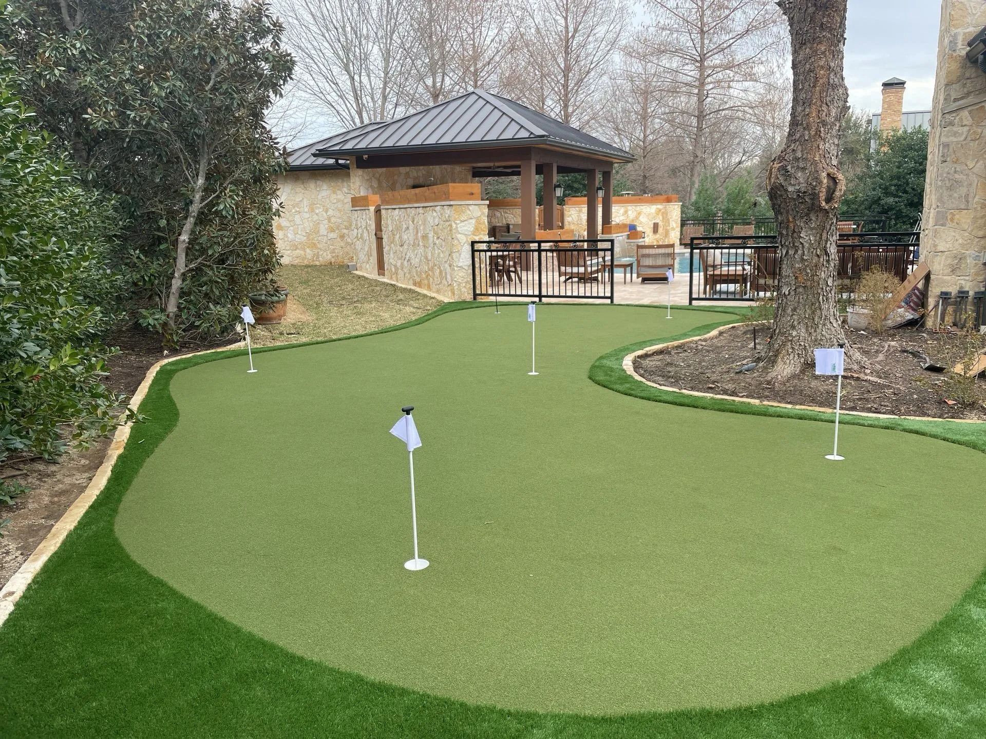 Mini golf green with two white flags beside a stone gazebo and trees